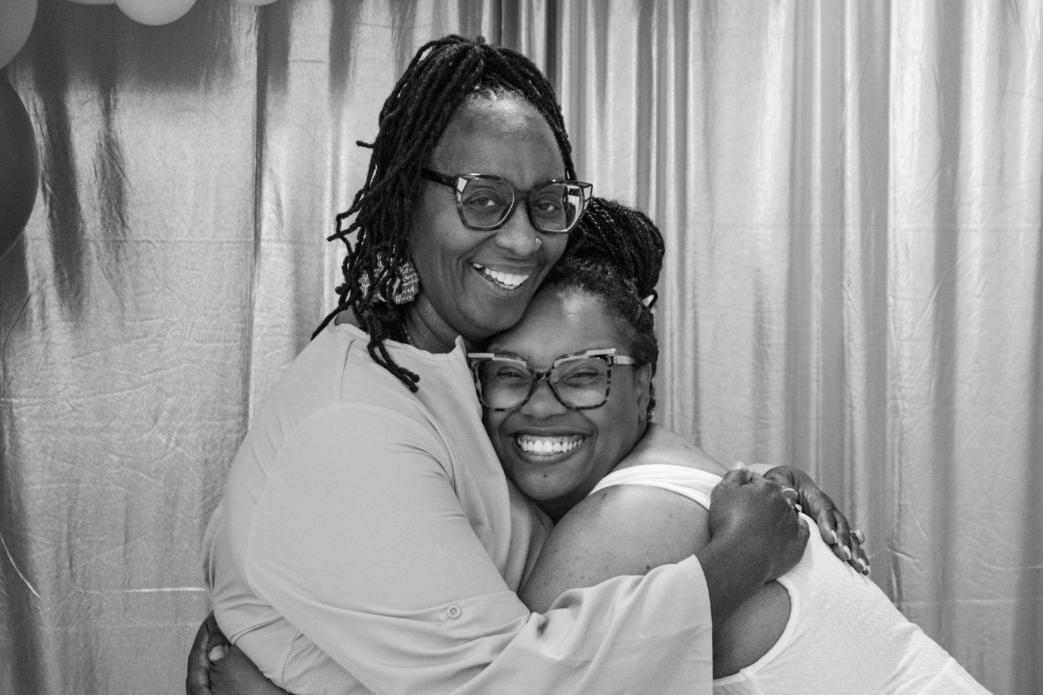 A black and white portrait of two people embracing at a celebration.
