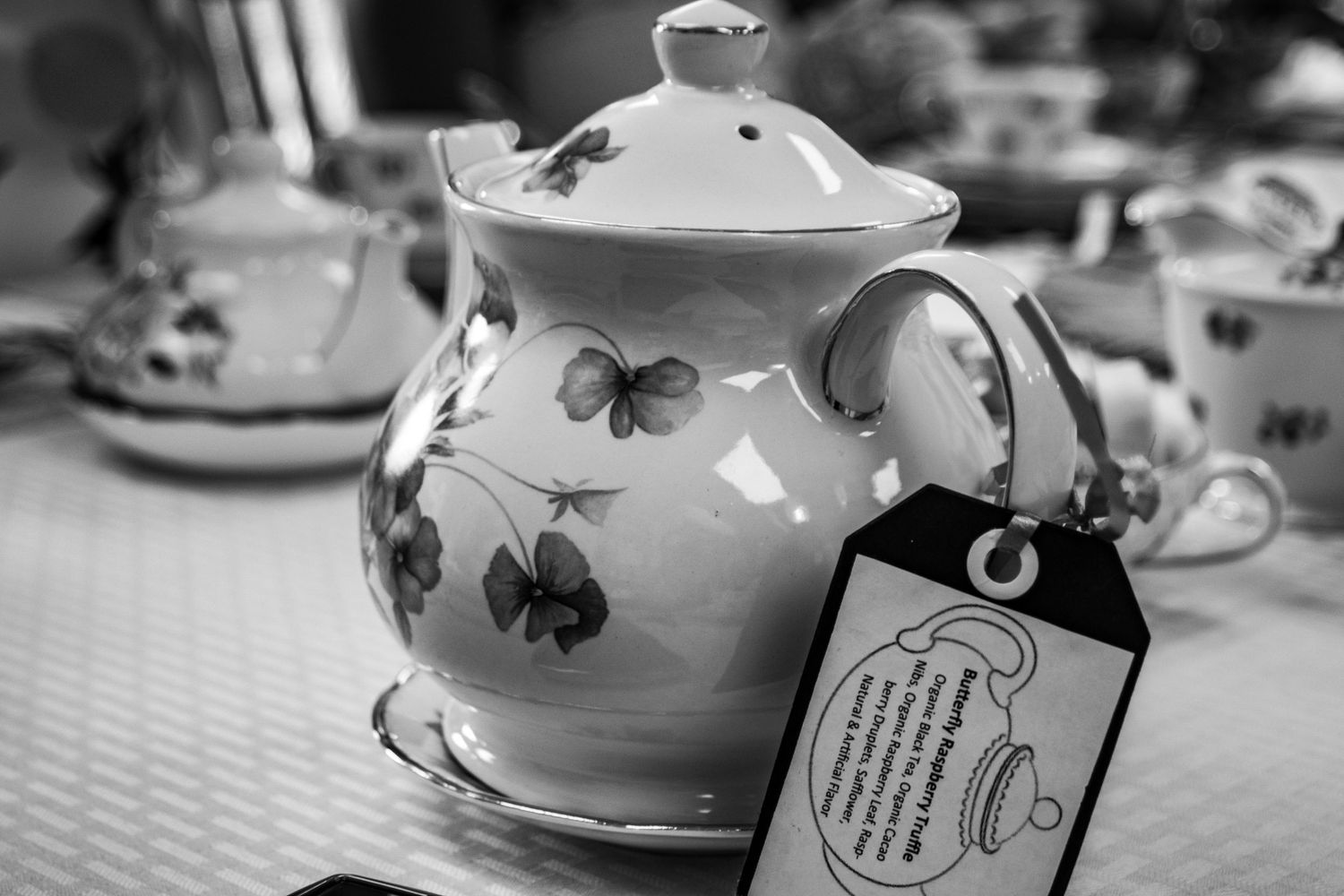 A white porcelain teapot with butterfly decorations and a hanging tag.