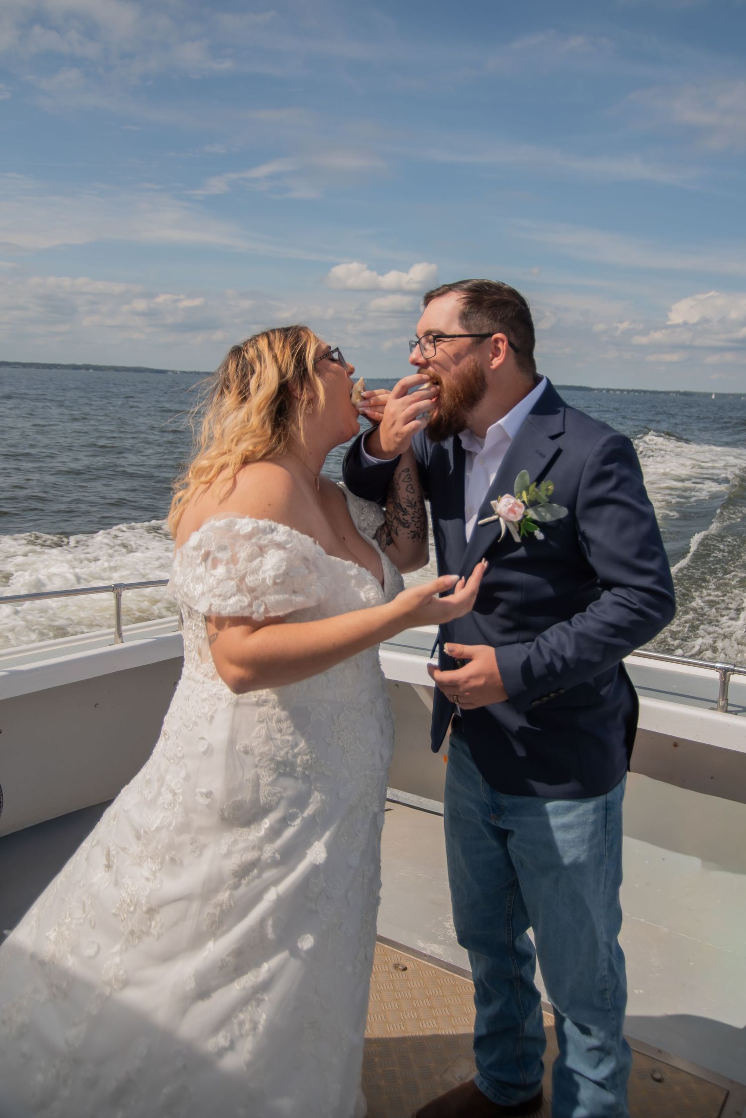 Bride and groom sharing a romantic cake feeding moment on a boat deck with ocean waves in the background.