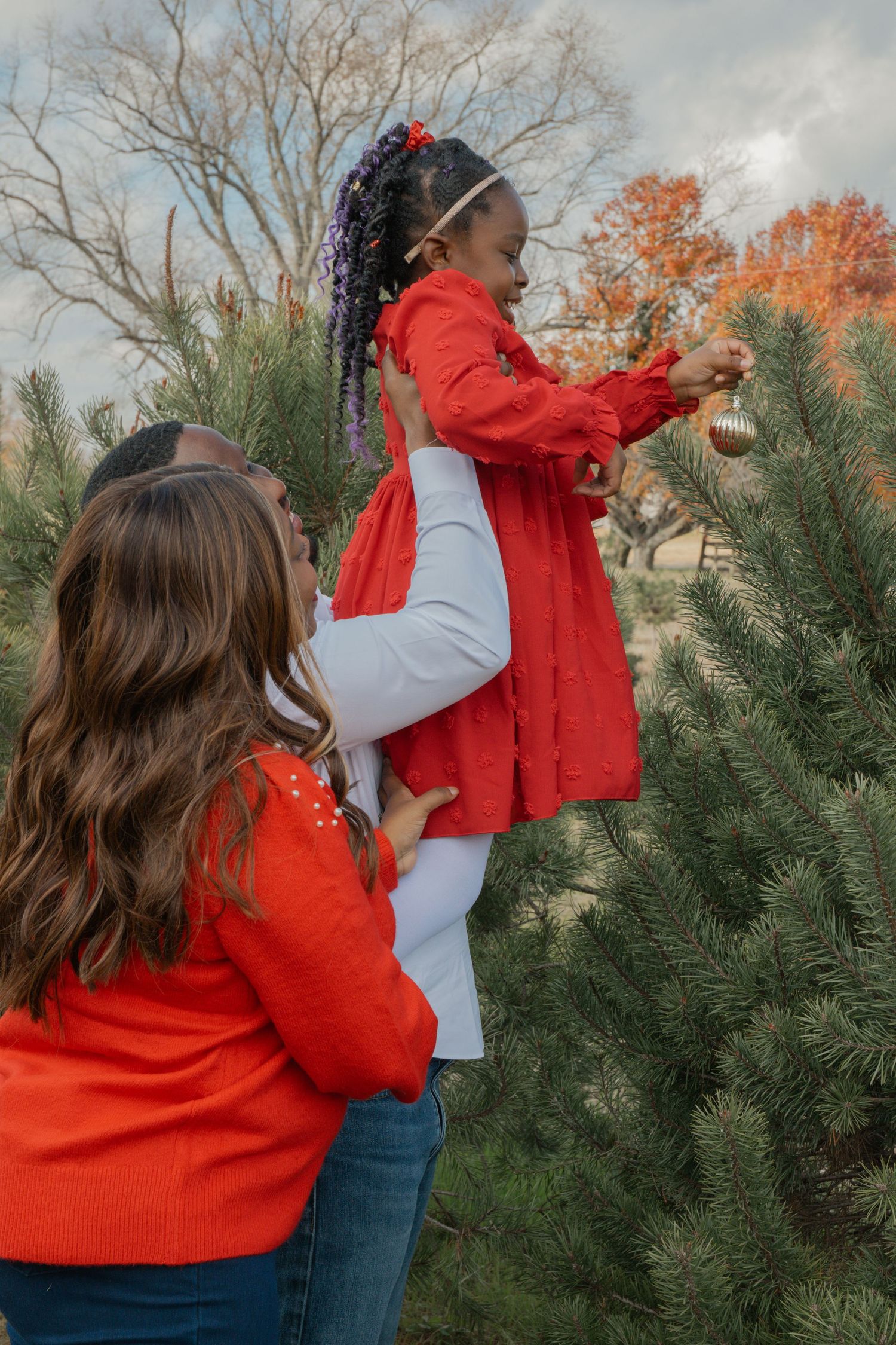 Family decorating a Christmas tree together outdoors in winter clothing.