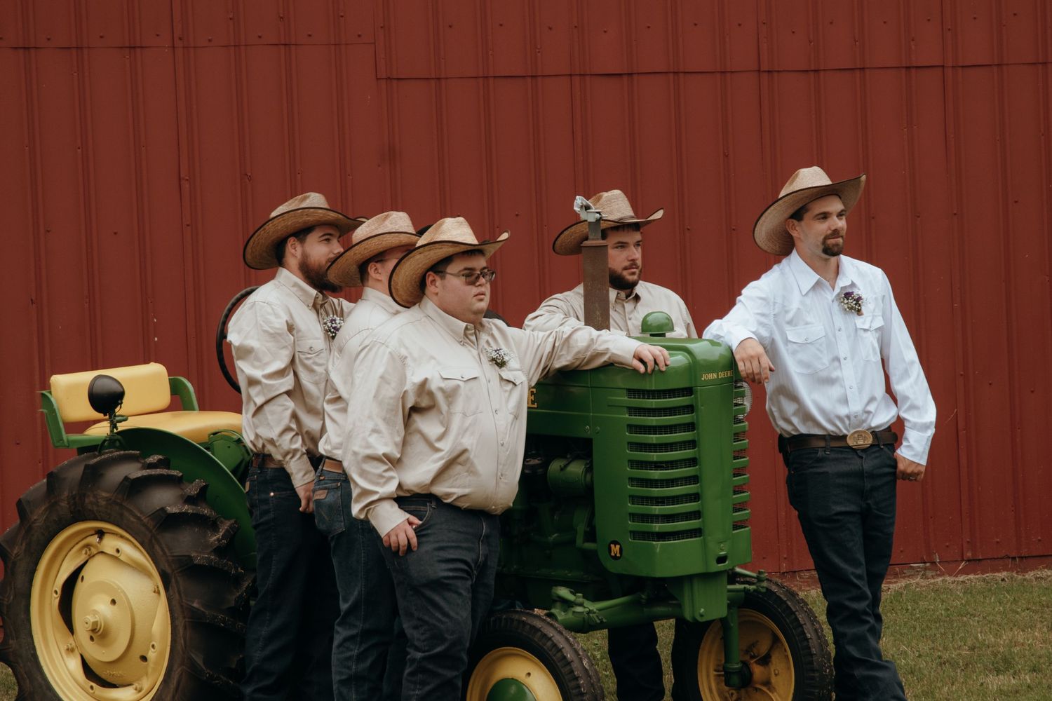 Wedding party gathered near a red barn with John Deere tractors in the background.