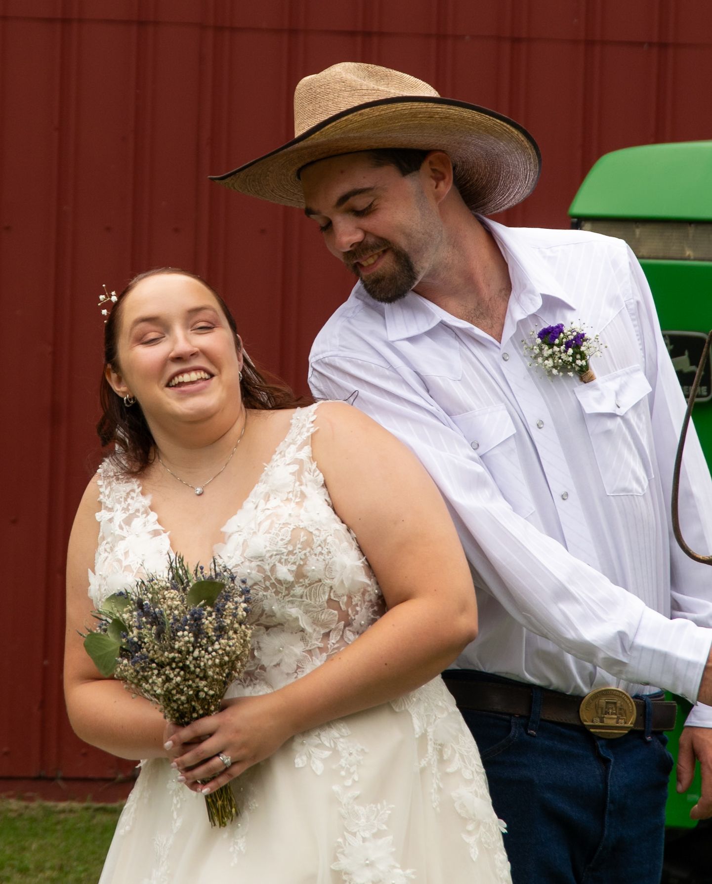 A couple shares a joyful moment at their rustic country wedding, with the bride in white lace holding a wildflower bouquet.