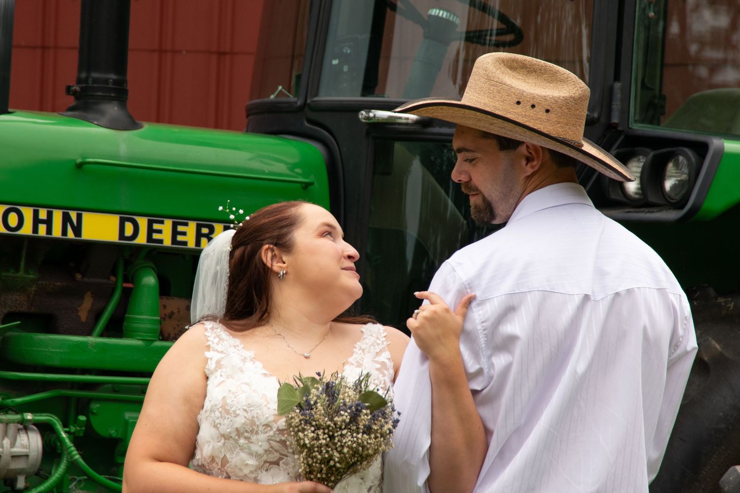 A couple shares a romantic moment during their wedding photos in front of a green John Deere tractor.
