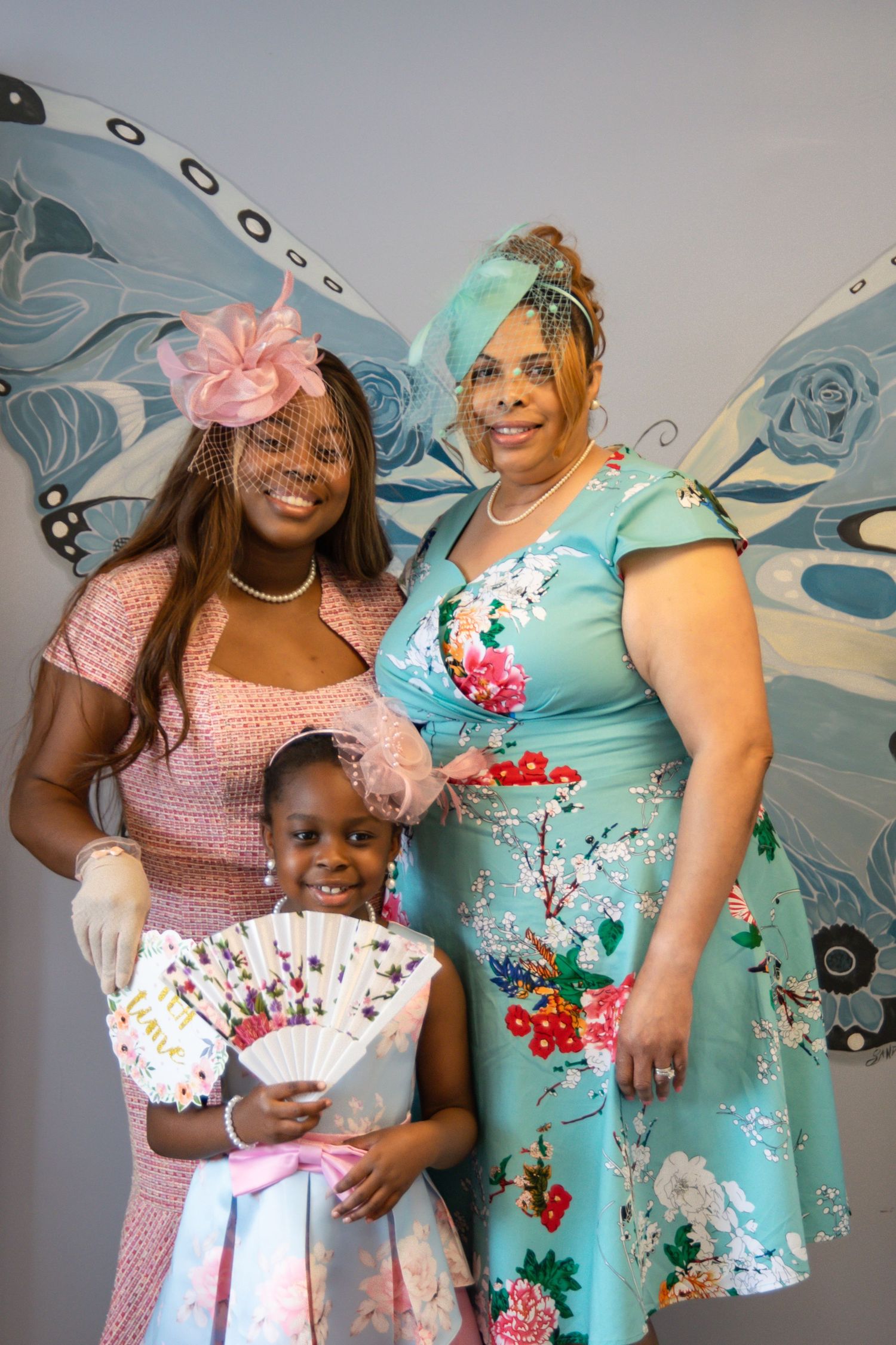 Guests in pastel dresses pose together against decorative blue butterfly wings backdrop.