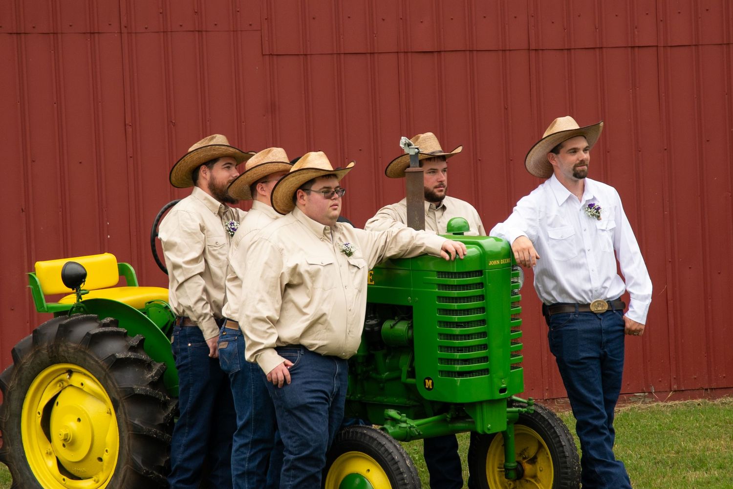 People gather around vintage John Deere tractors displayed in front of a red barn at an agricultural show.