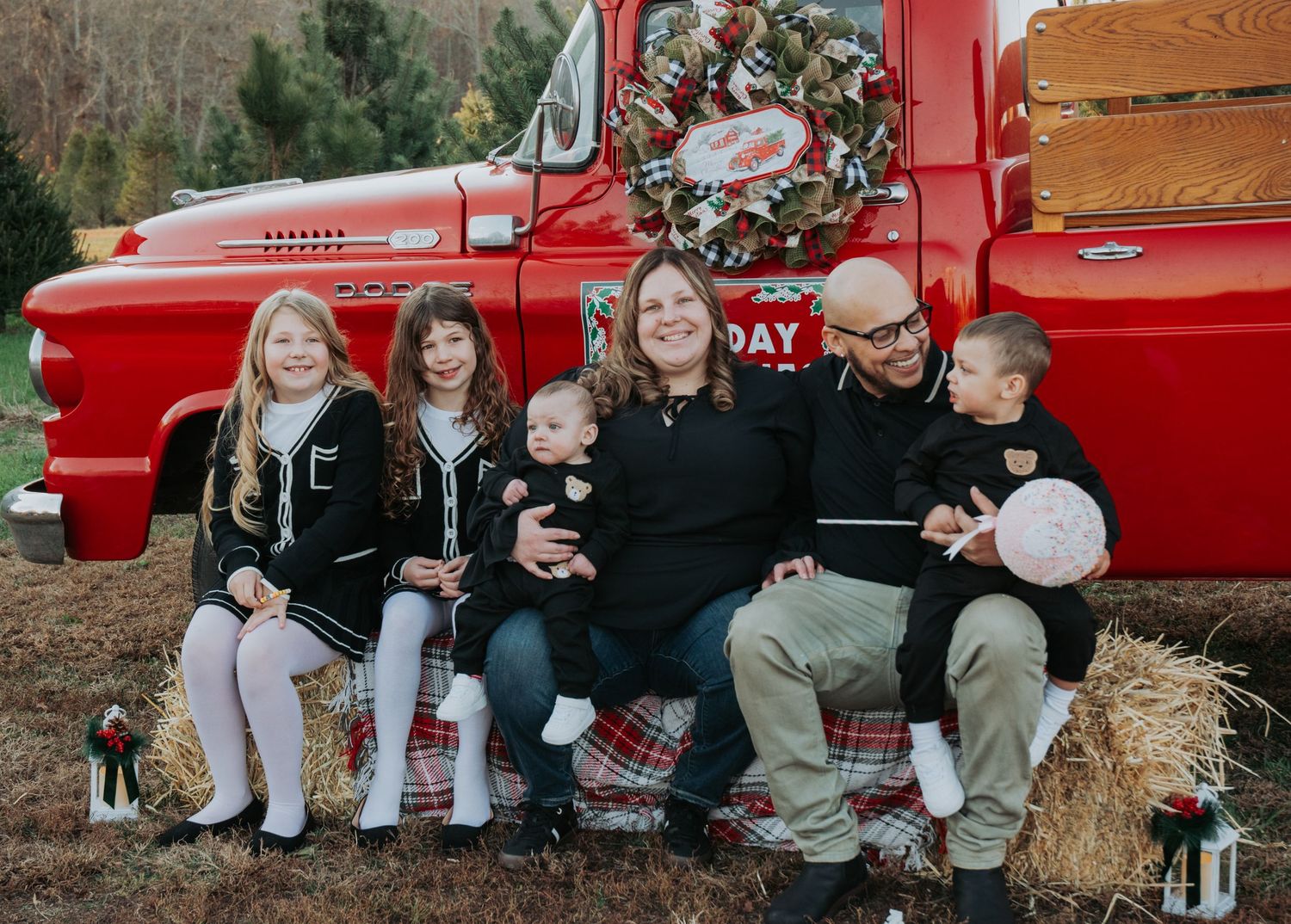 Family poses on hay bales next to a vintage red pickup truck during an autumn photoshoot.