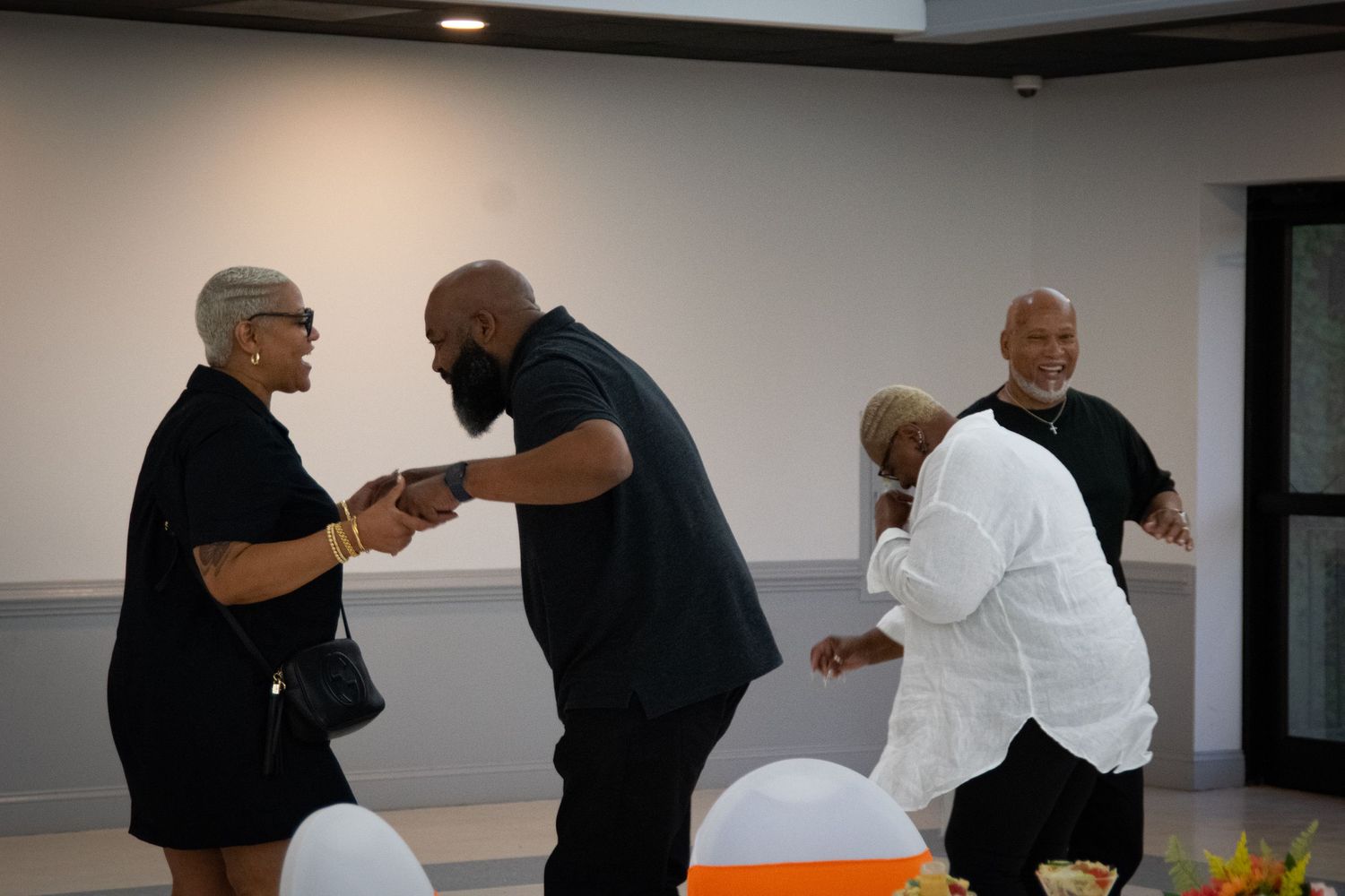 People dancing and celebrating at an indoor retirement party with white chairs.