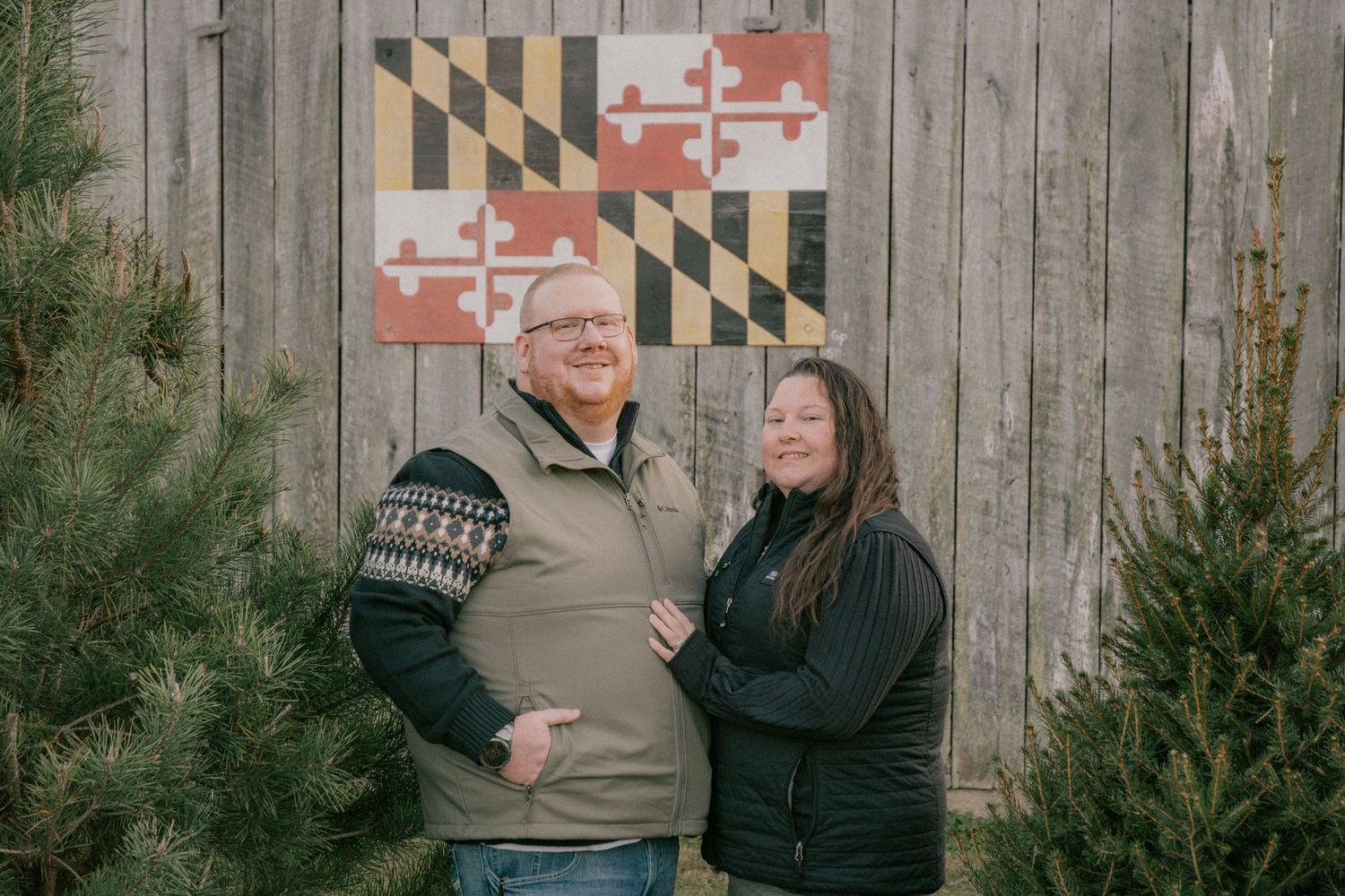 Couple posing playfully in front of a wooden fence with Maryland flag design.