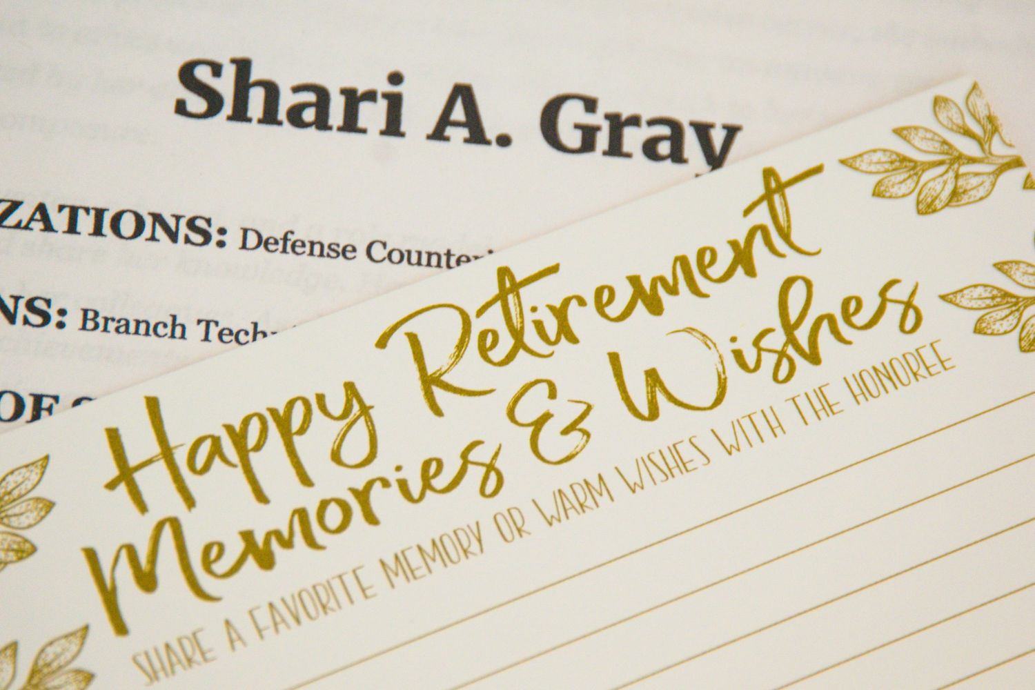 A retirement card with gold lettering saying 'Happy Retirement Memories & Wishes'.