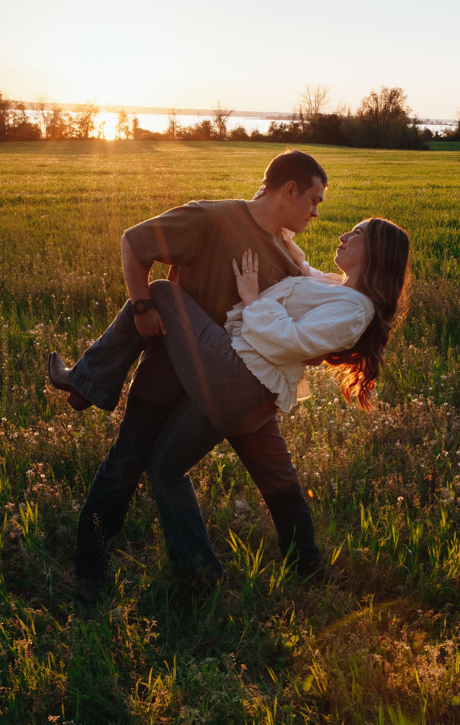 Couple dancing romantically in a sunlit green field at golden hour, man dipping woman gracefully.