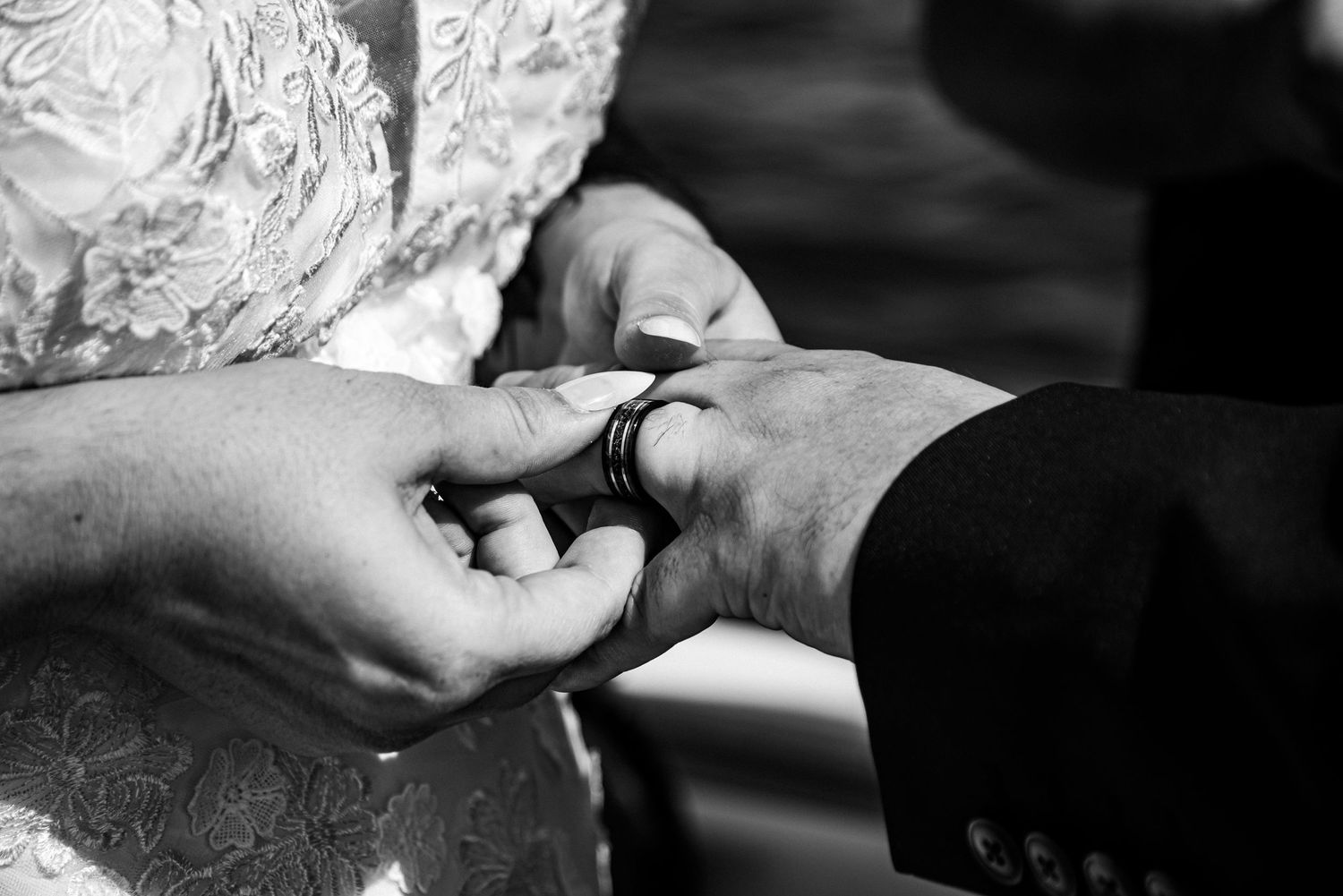 Black and white photo of a bride placing a wedding ring on the groom's finger during a wedding ceremony.