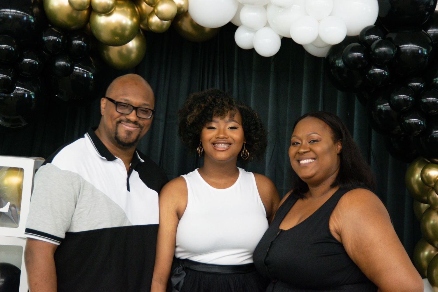 Celebration photo with black, gold and white balloon arch backdrop.