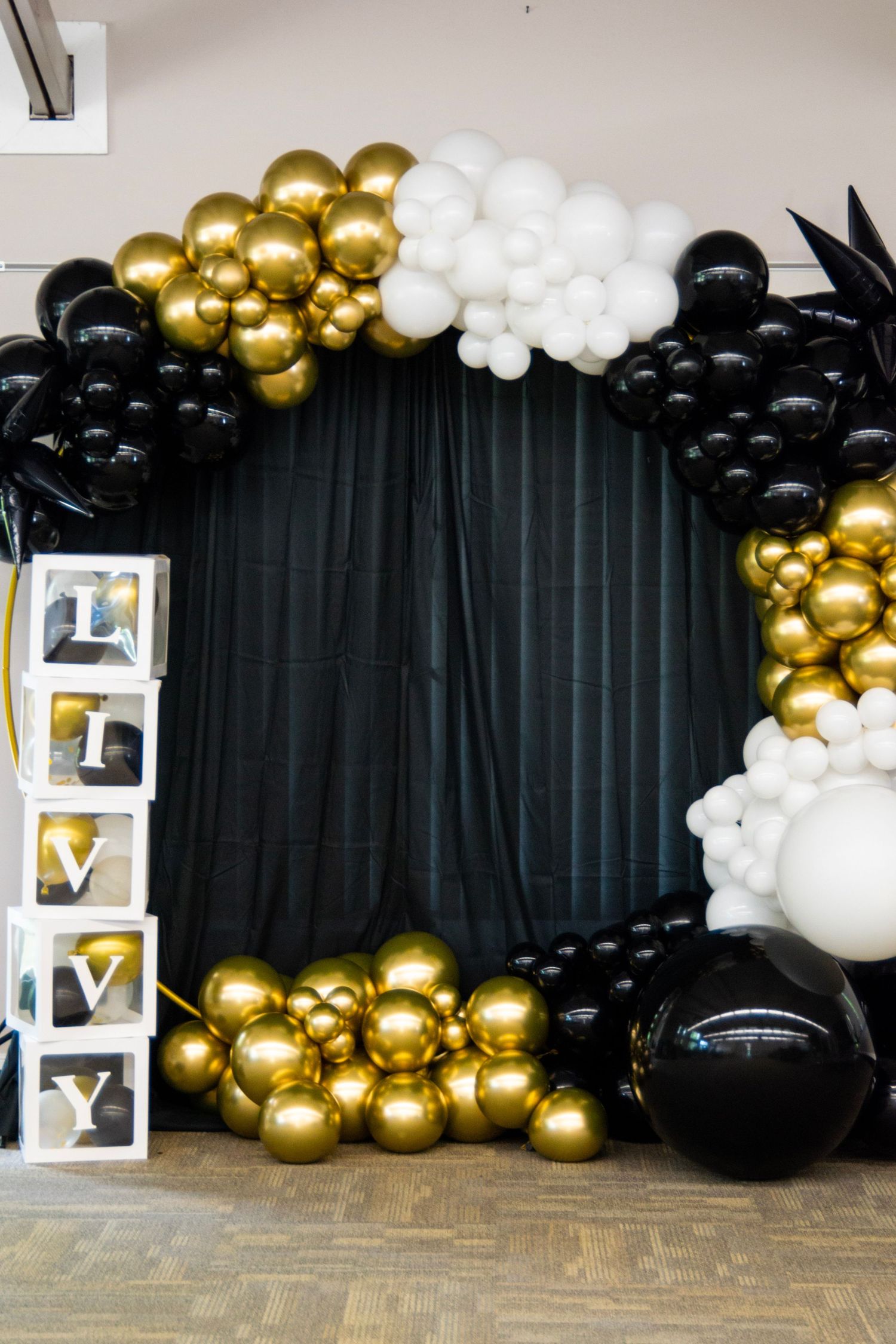 Elegant balloon arch in black, gold, and white colors with decorative light-up boxes.