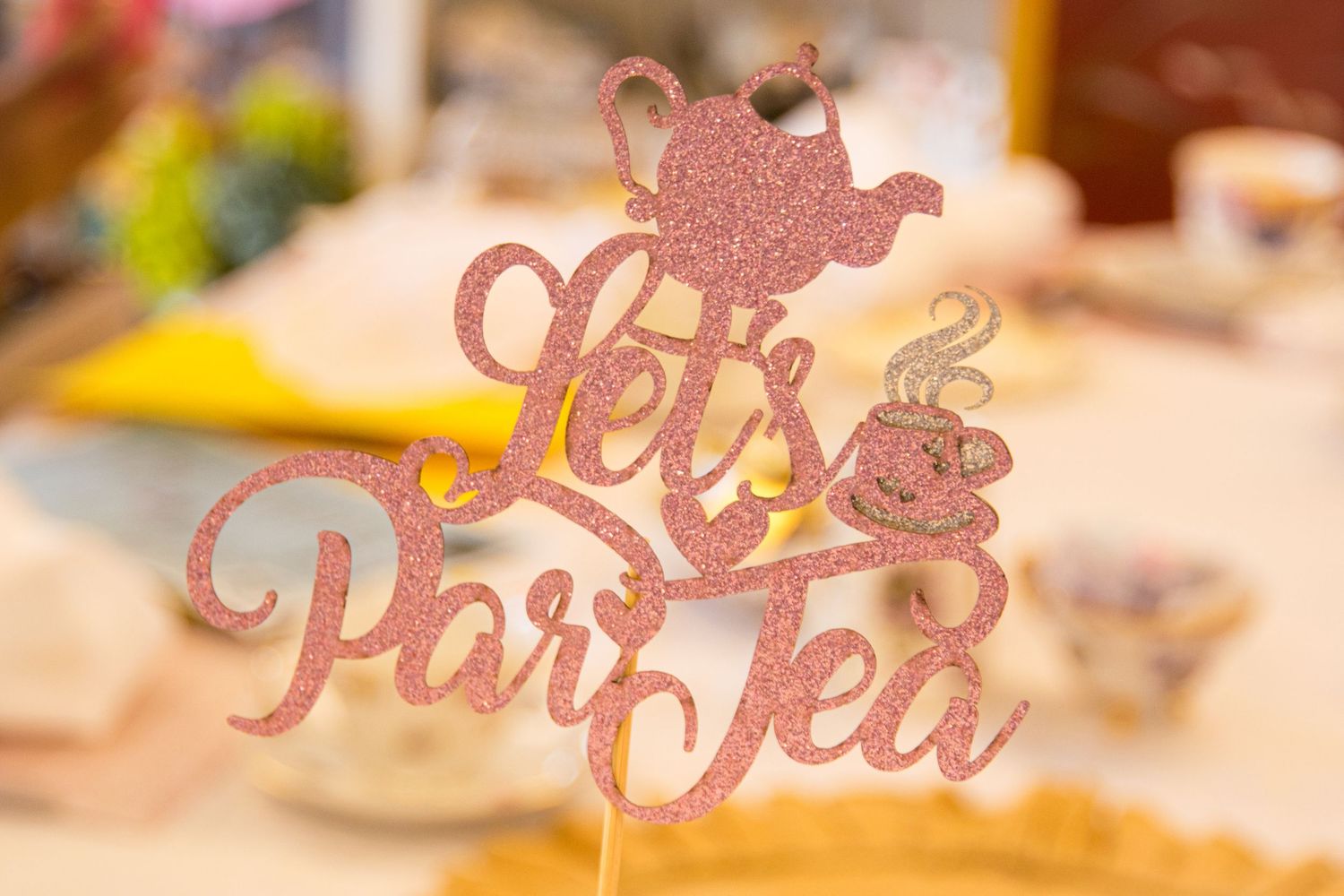 A glittery pink 'Let's Par-Tea' party sign decoration with a teapot silhouette.