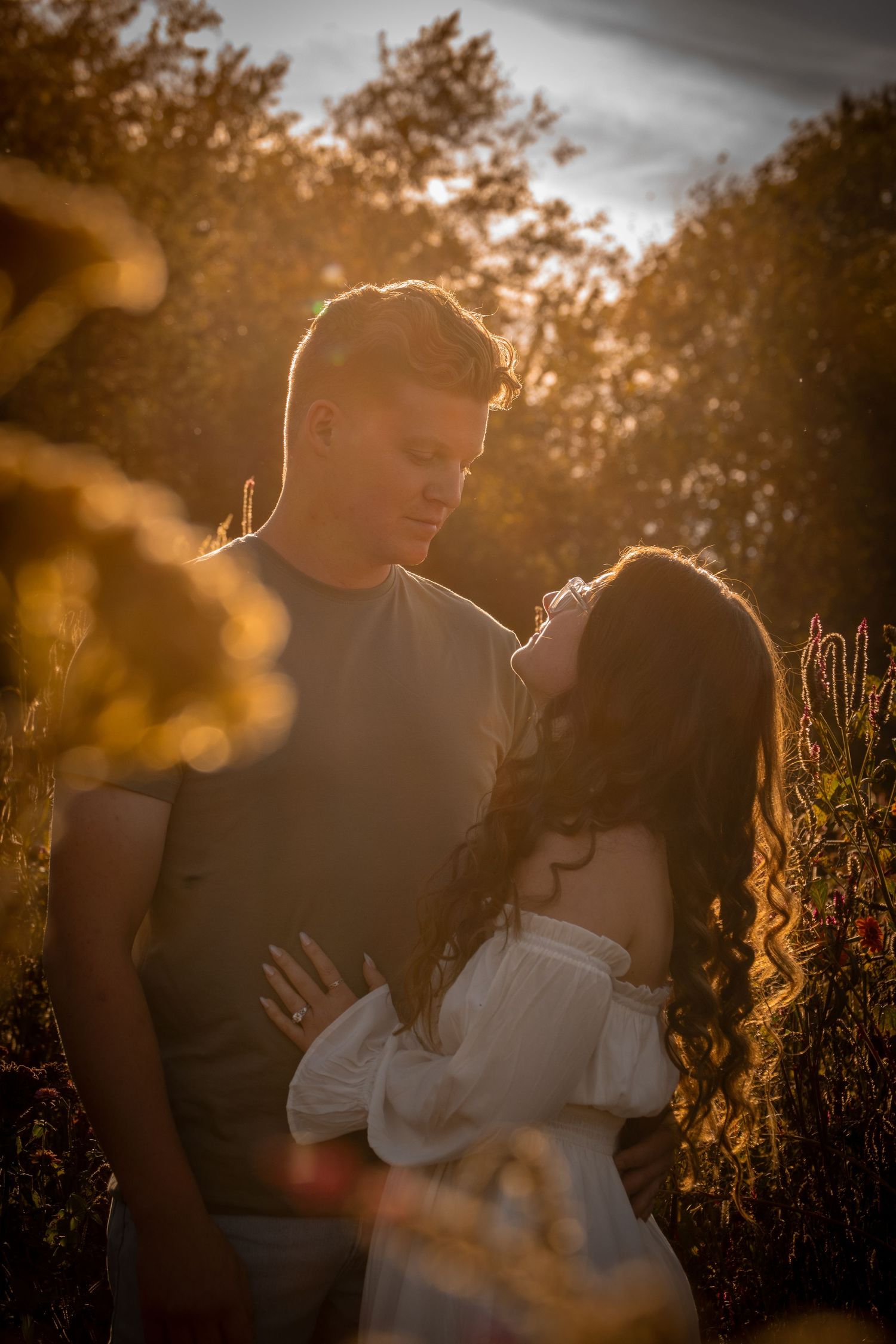 Romantic couple embracing in a golden sunset with backlit silhouettes among trees.