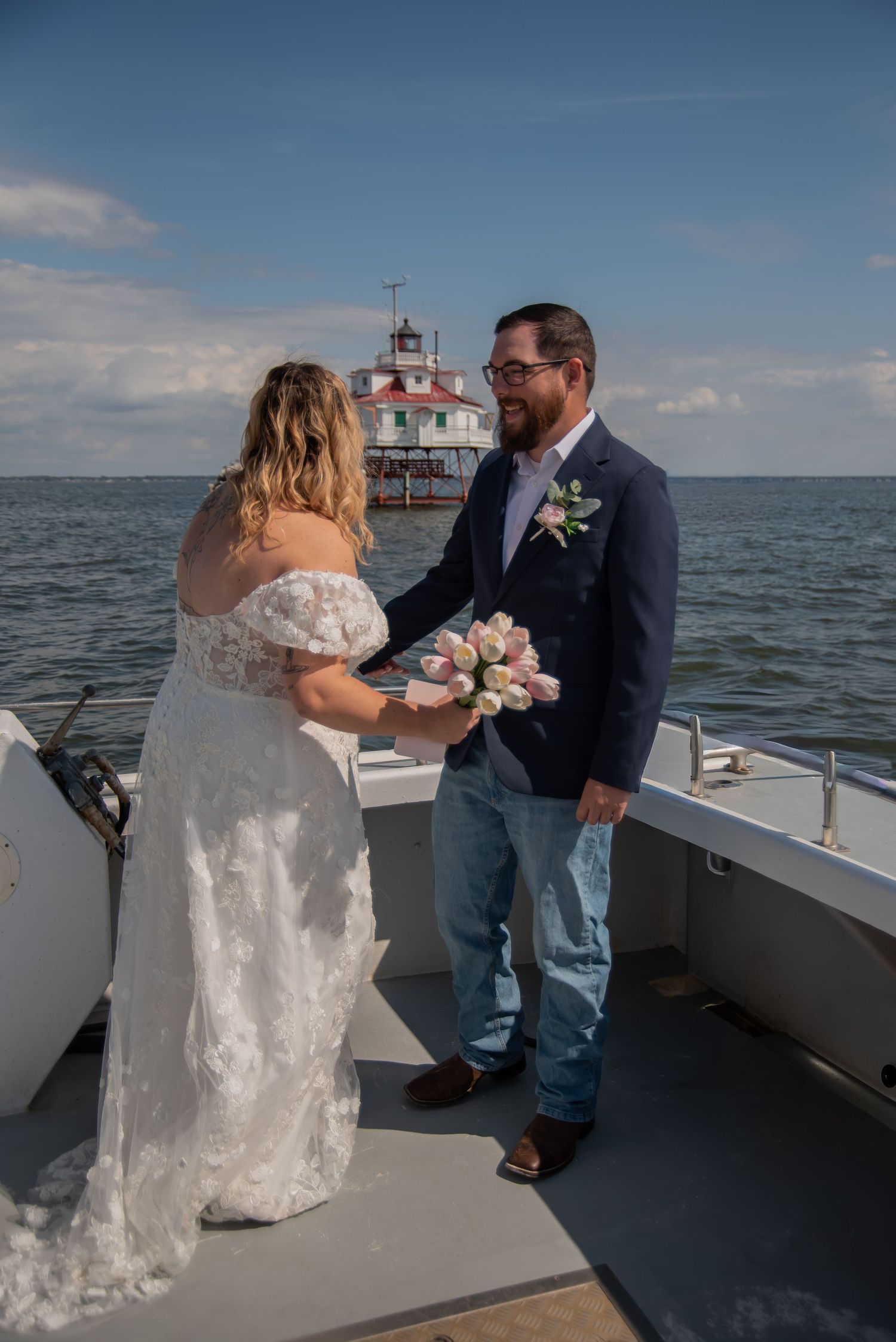 Couple exchanging vows on a boat deck with a lighthouse and blue sky in the background on their wedding day.
