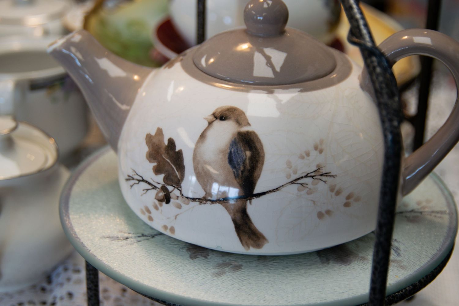 A white ceramic teapot decorated with a painted bird design sitting on a saucer.