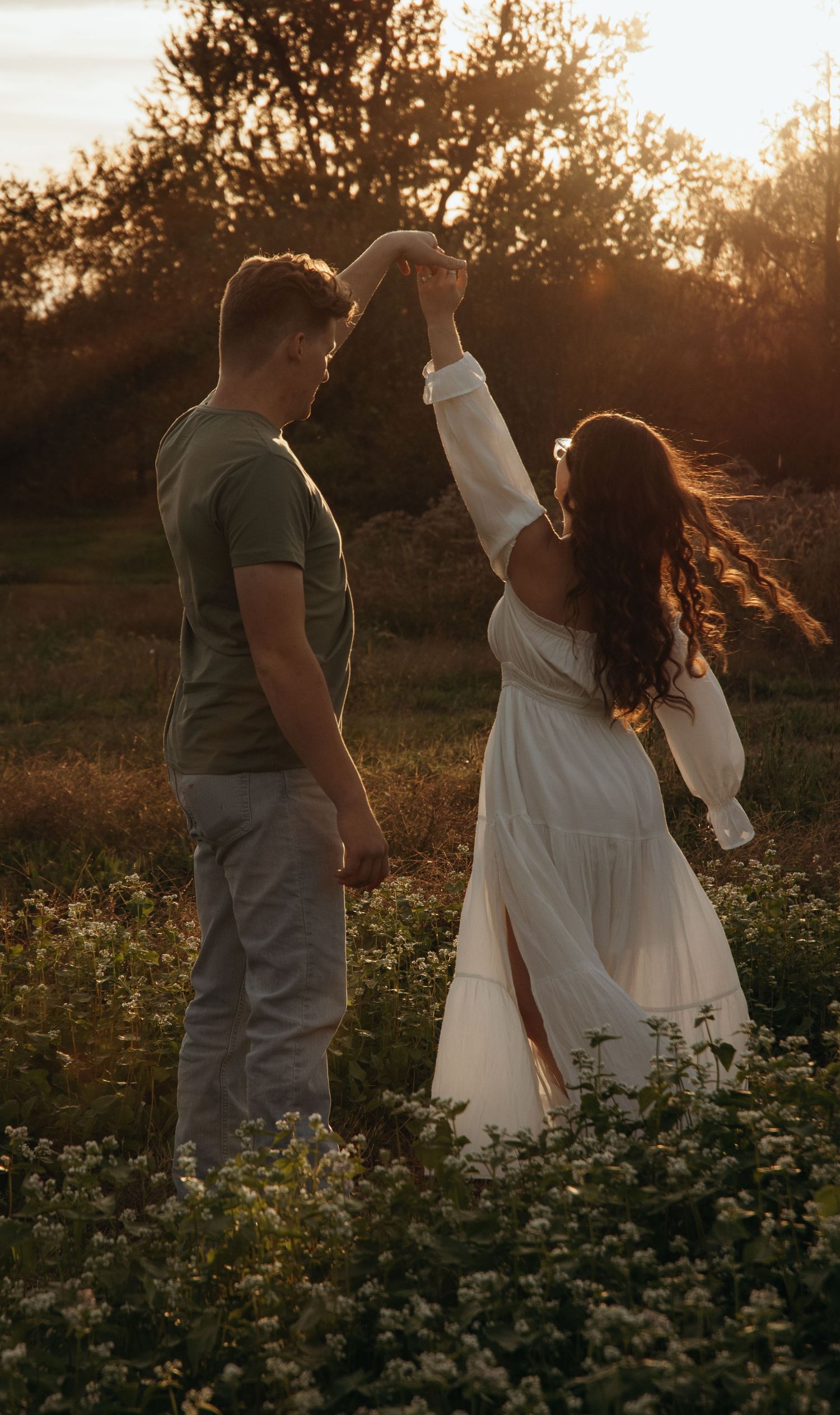 Couple walking through a flower field at sunset with golden light streaming through.
