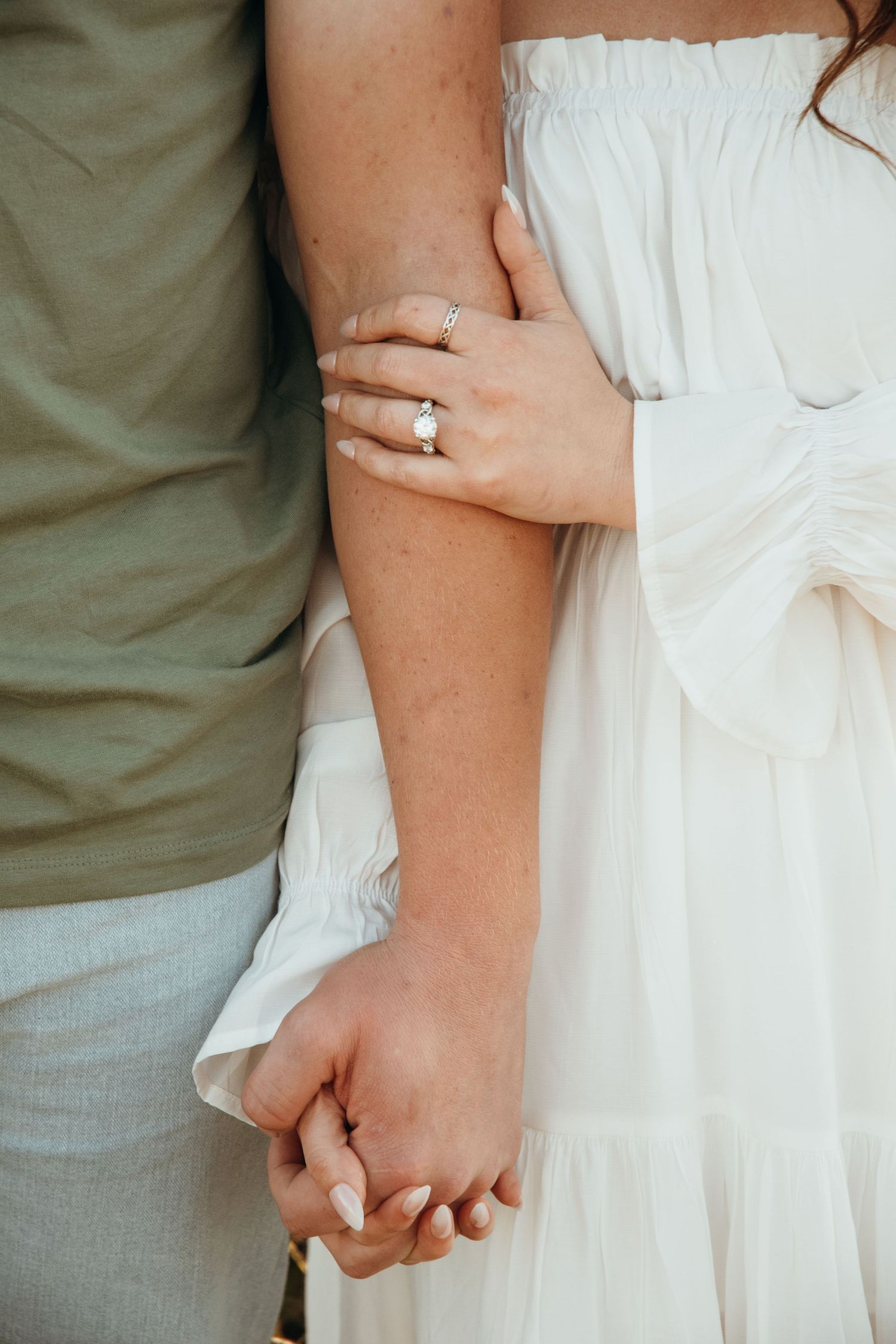 Close-up details of white dress and gentle embrace during engagement photoshoot.