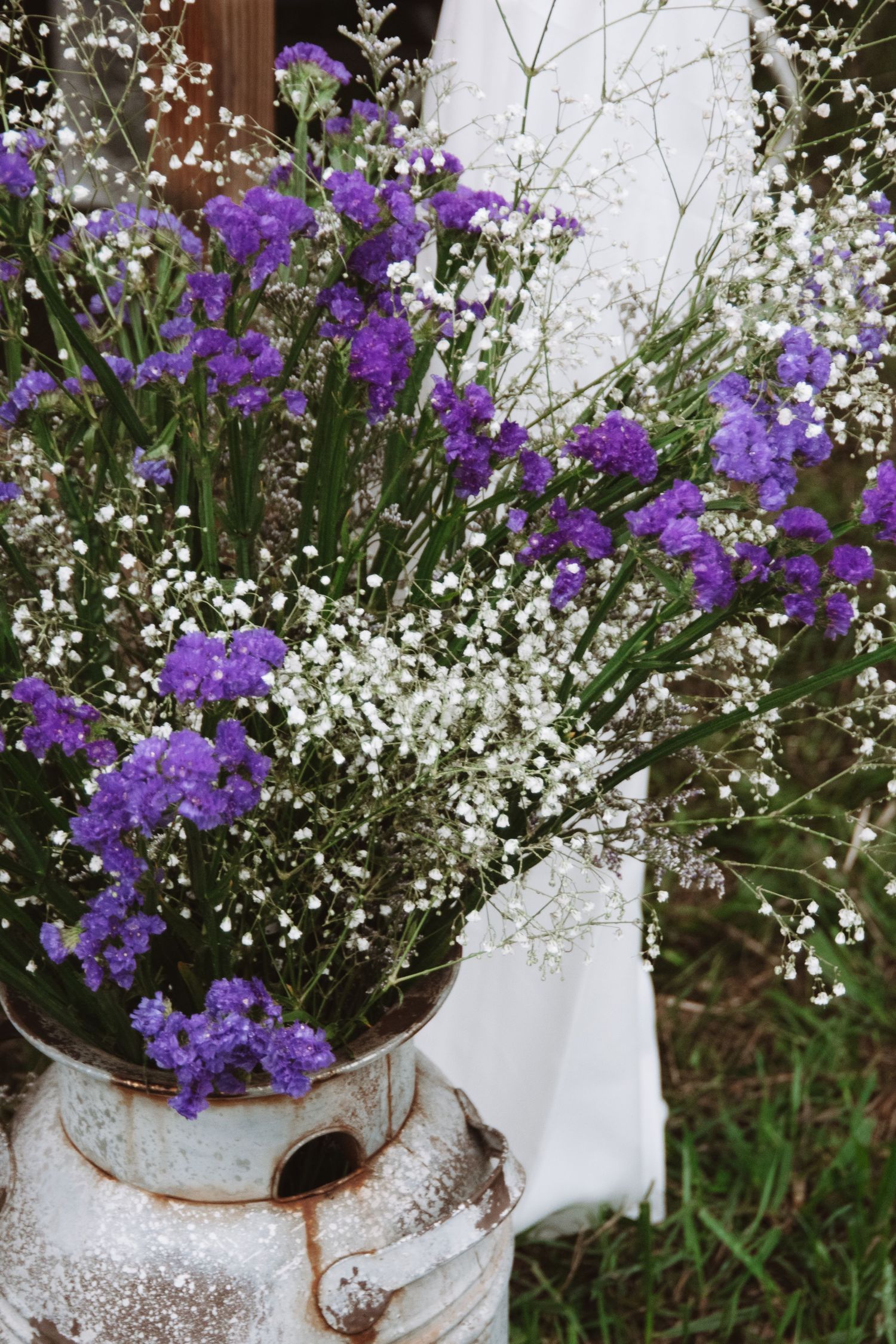 Purple campanula flowers and delicate white baby's breath arranged in a rustic white ceramic container.