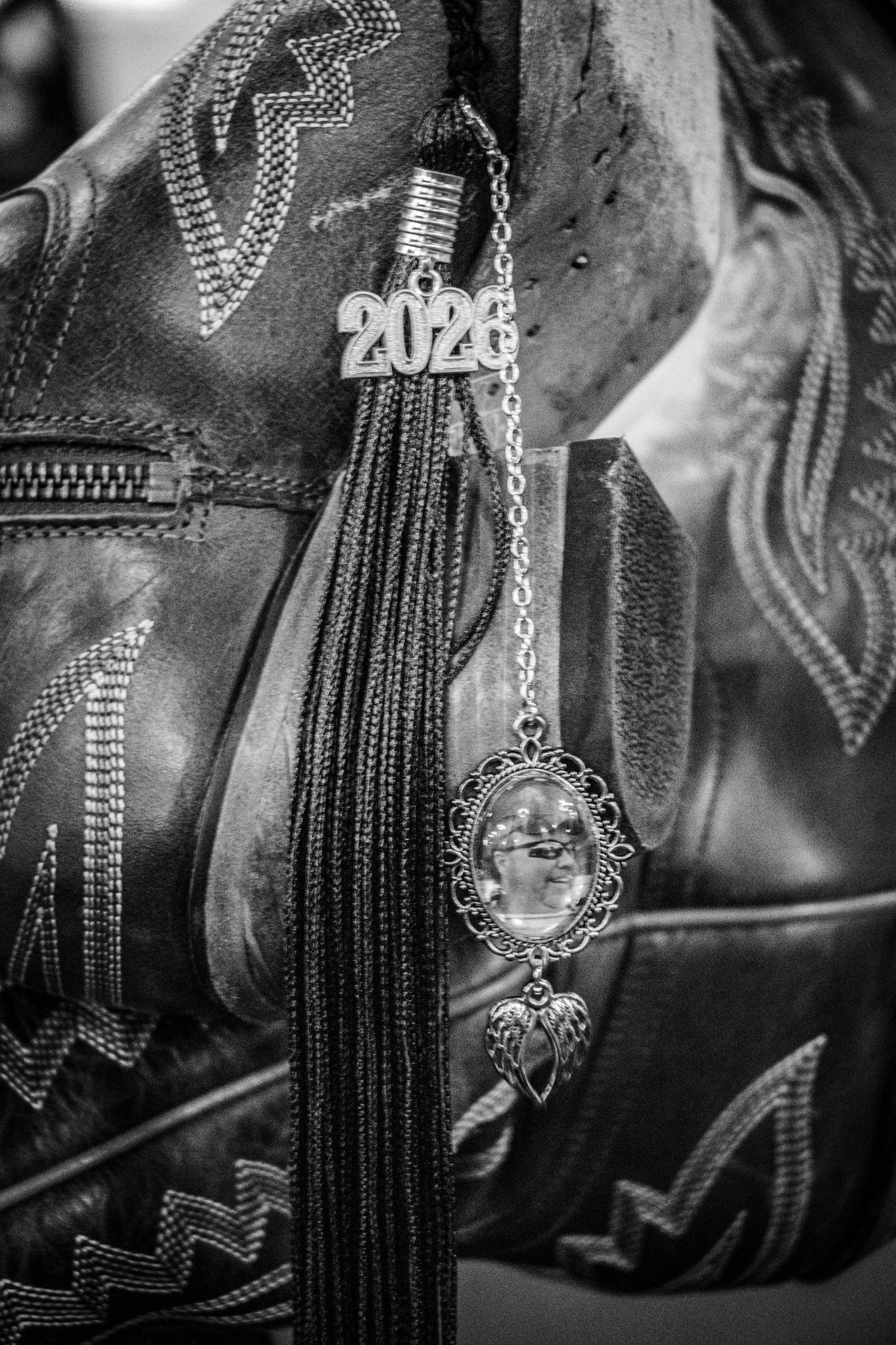 Black and white photo of a 2026 graduation tassel with a memorial photo charm hanging on leather cowboy boots.