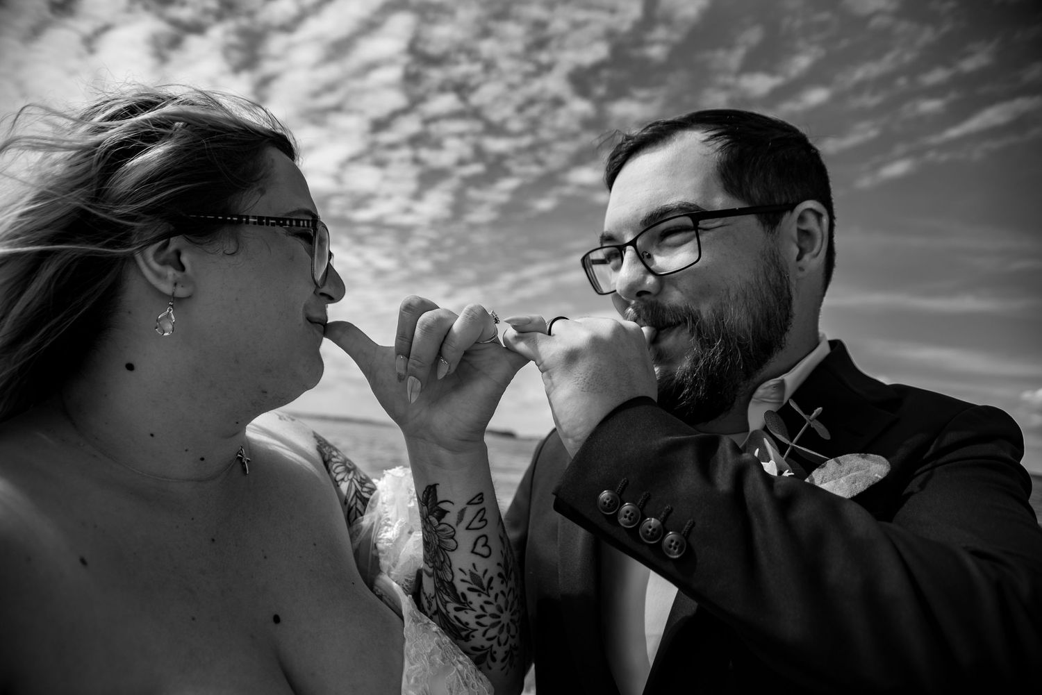 Black and white photo of a couple sharing a kiss during their wedding cake cutting ceremony outdoors.