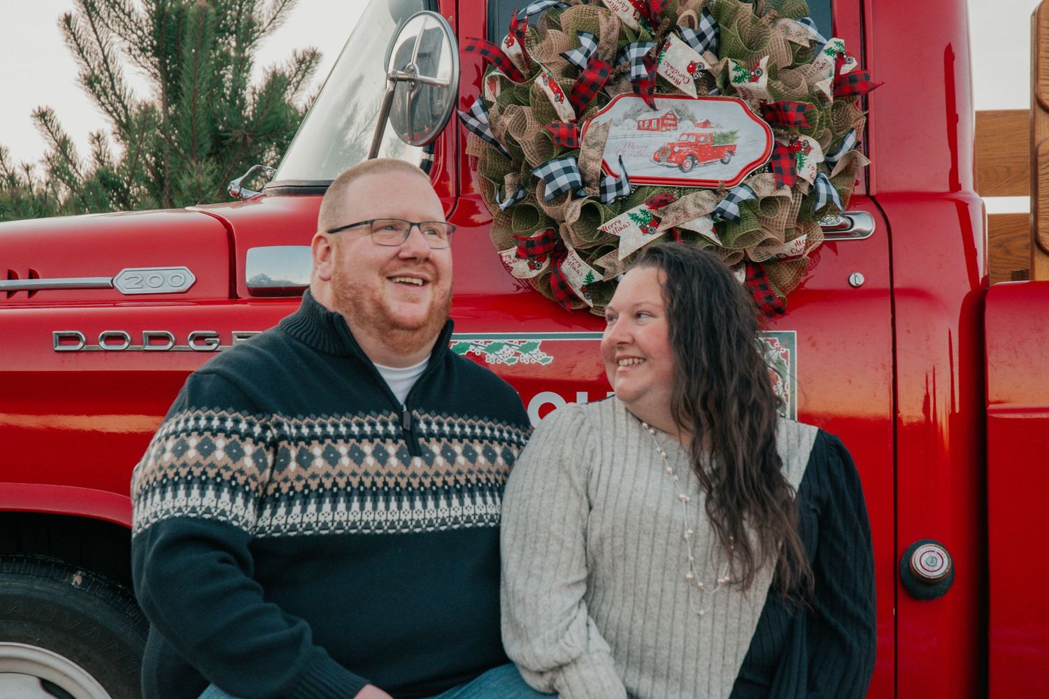 Couple sharing joyful moments in front of a red vintage truck with Christmas decorations.