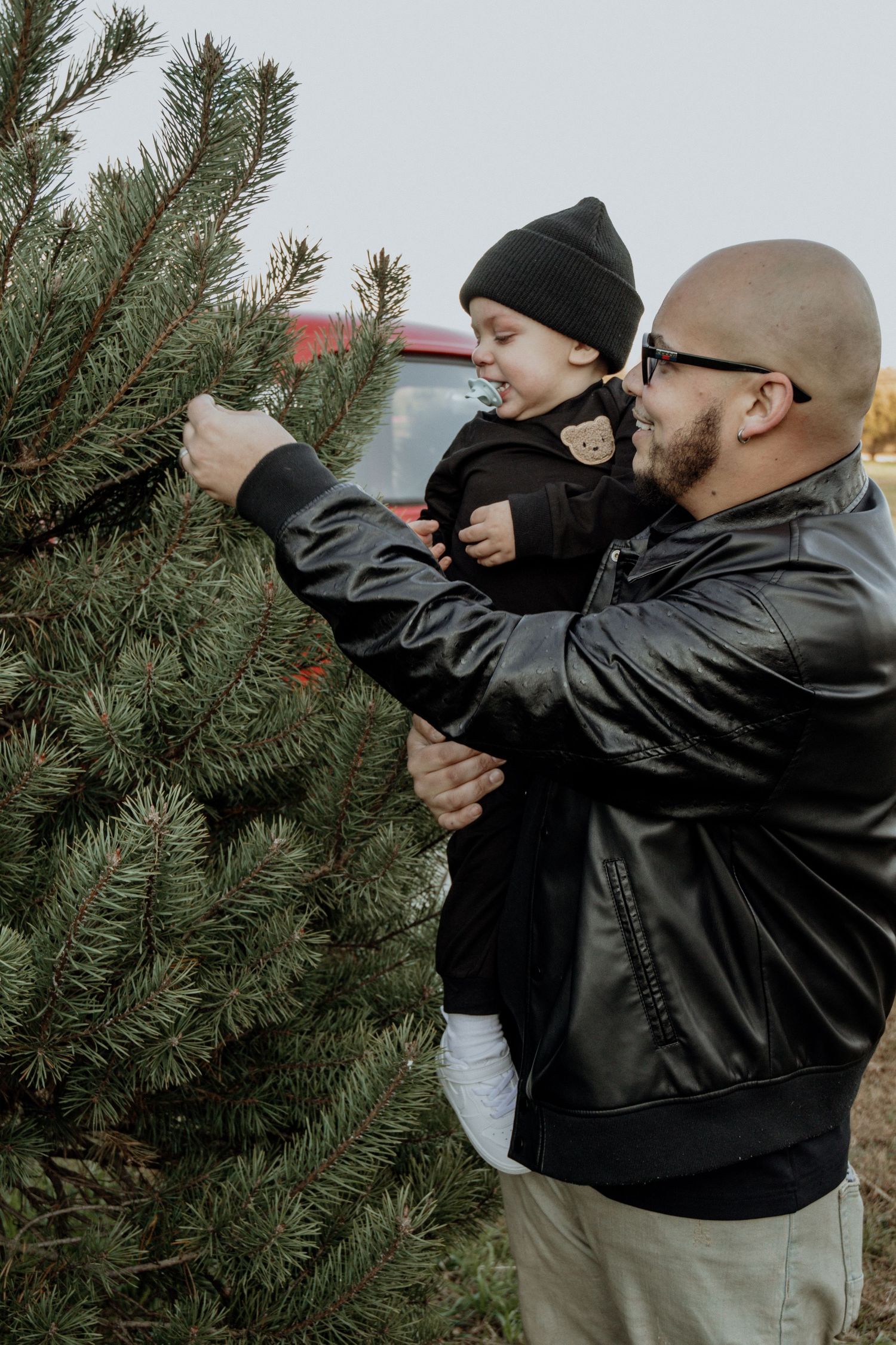 Two people decorating a large Christmas tree with ornaments at a tree farm.