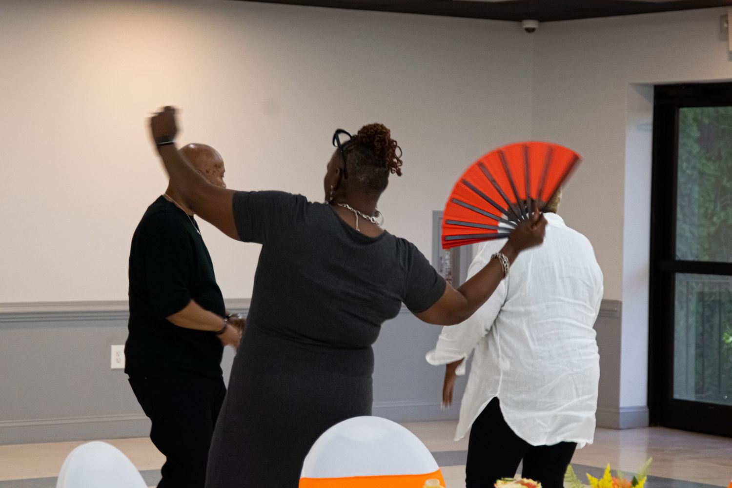Party guests dancing and celebrating with decorative fans at an indoor event.