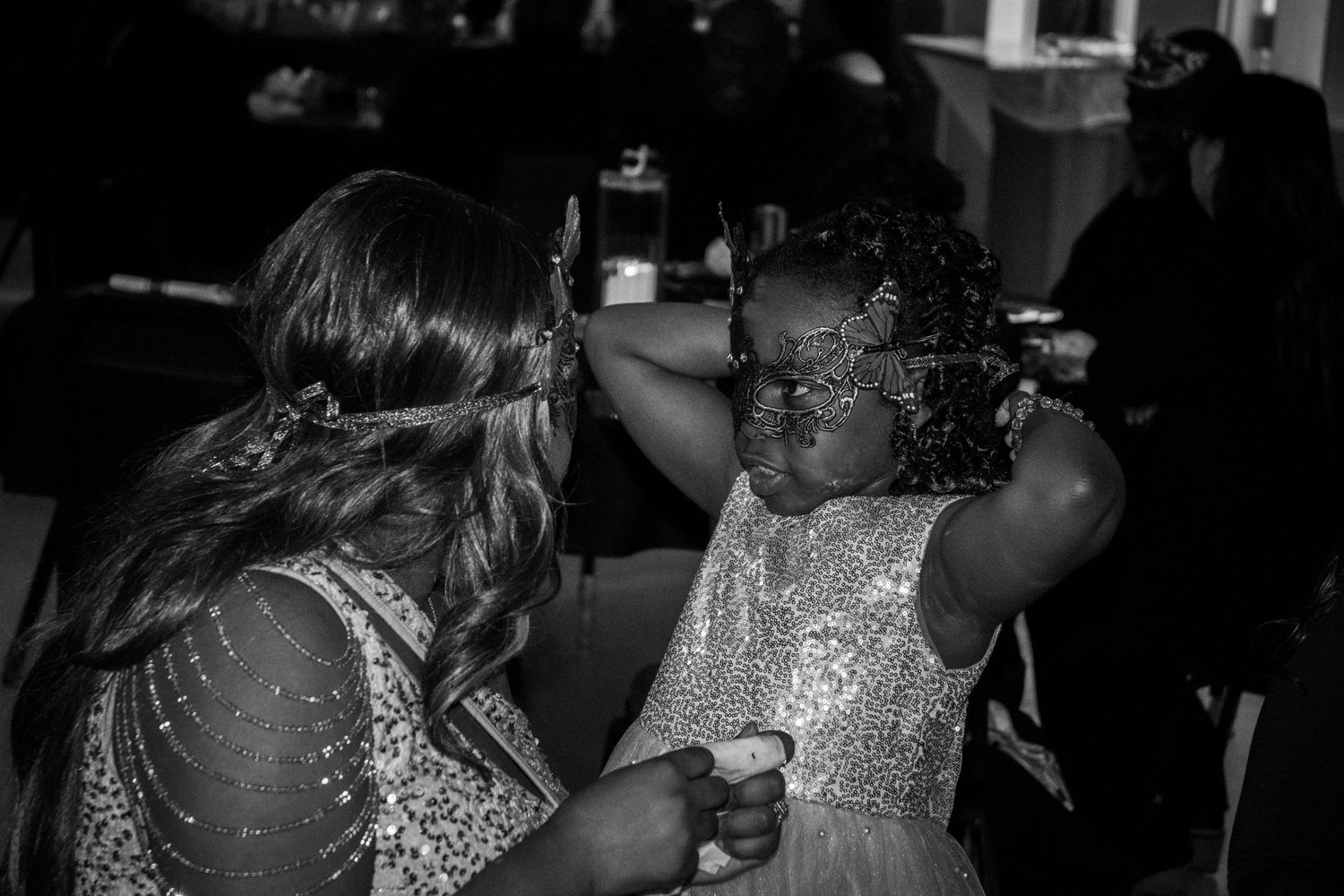 Guests in sequined dresses and masks mingle at a dimly lit formal event.