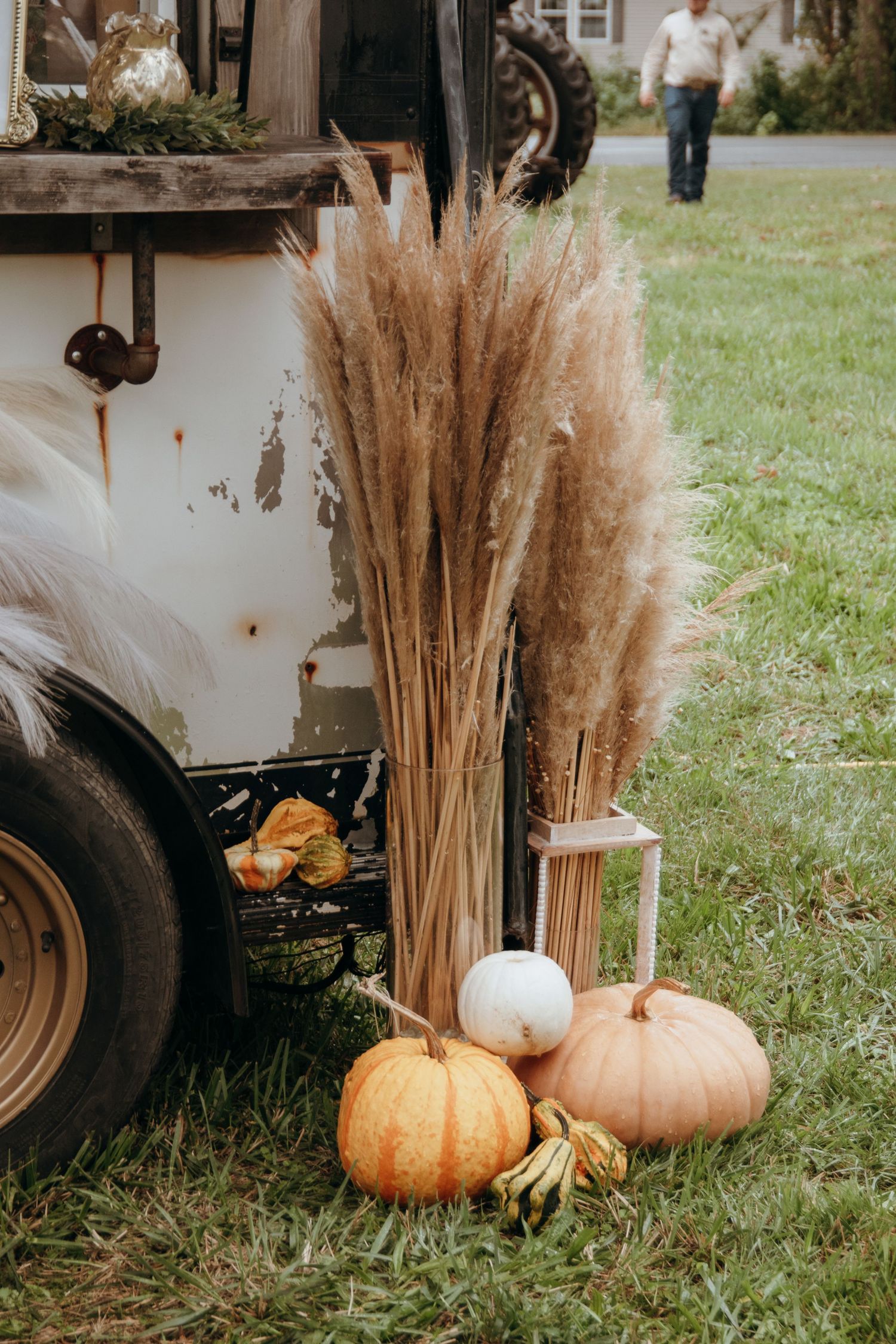 Fall wedding decor with pumpkins and dried wheat stalks arranged against a white vintage backdrop.