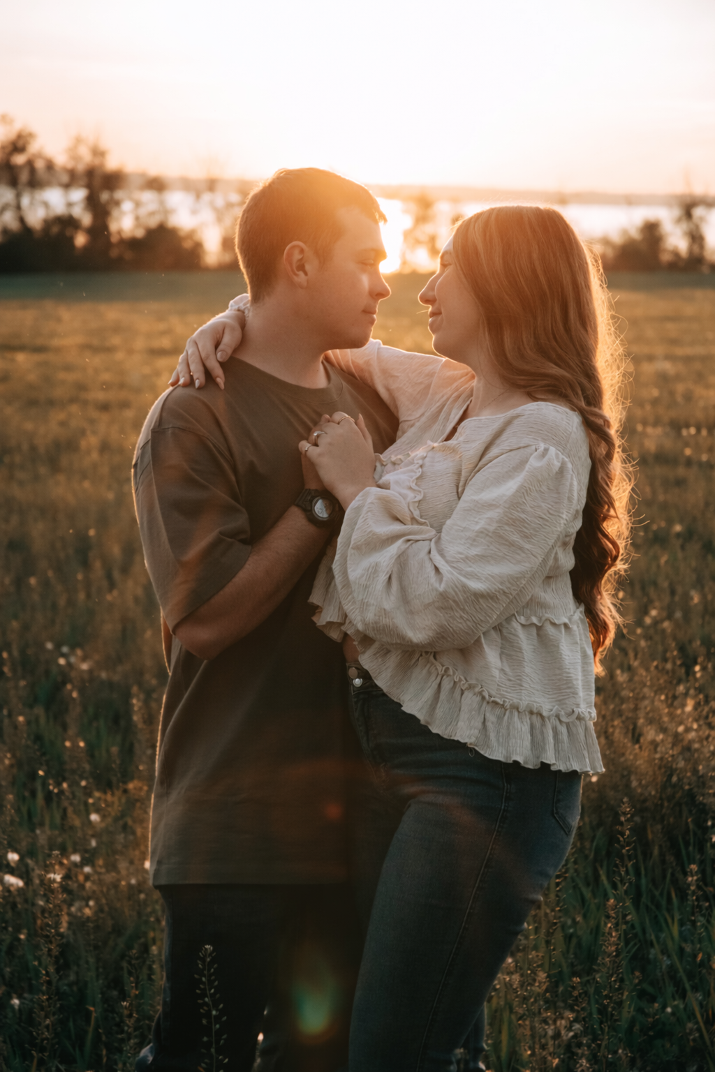 Couple embracing in golden sunset field, sharing a romantic moment with warm backlit glow and lush green meadow backdrop.
