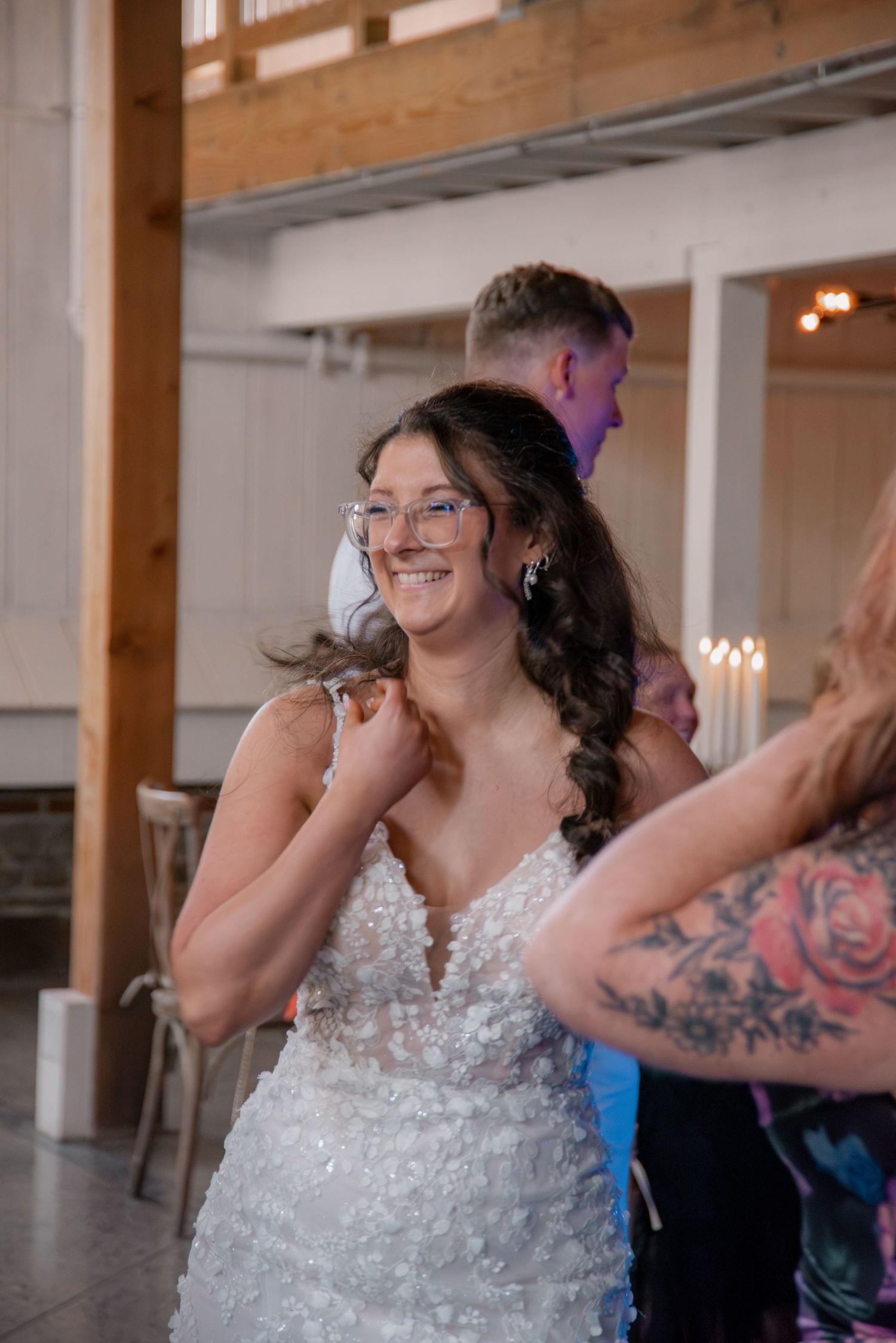 Smiling bride in a floral lace wedding gown and glasses dancing joyfully at her wedding reception.