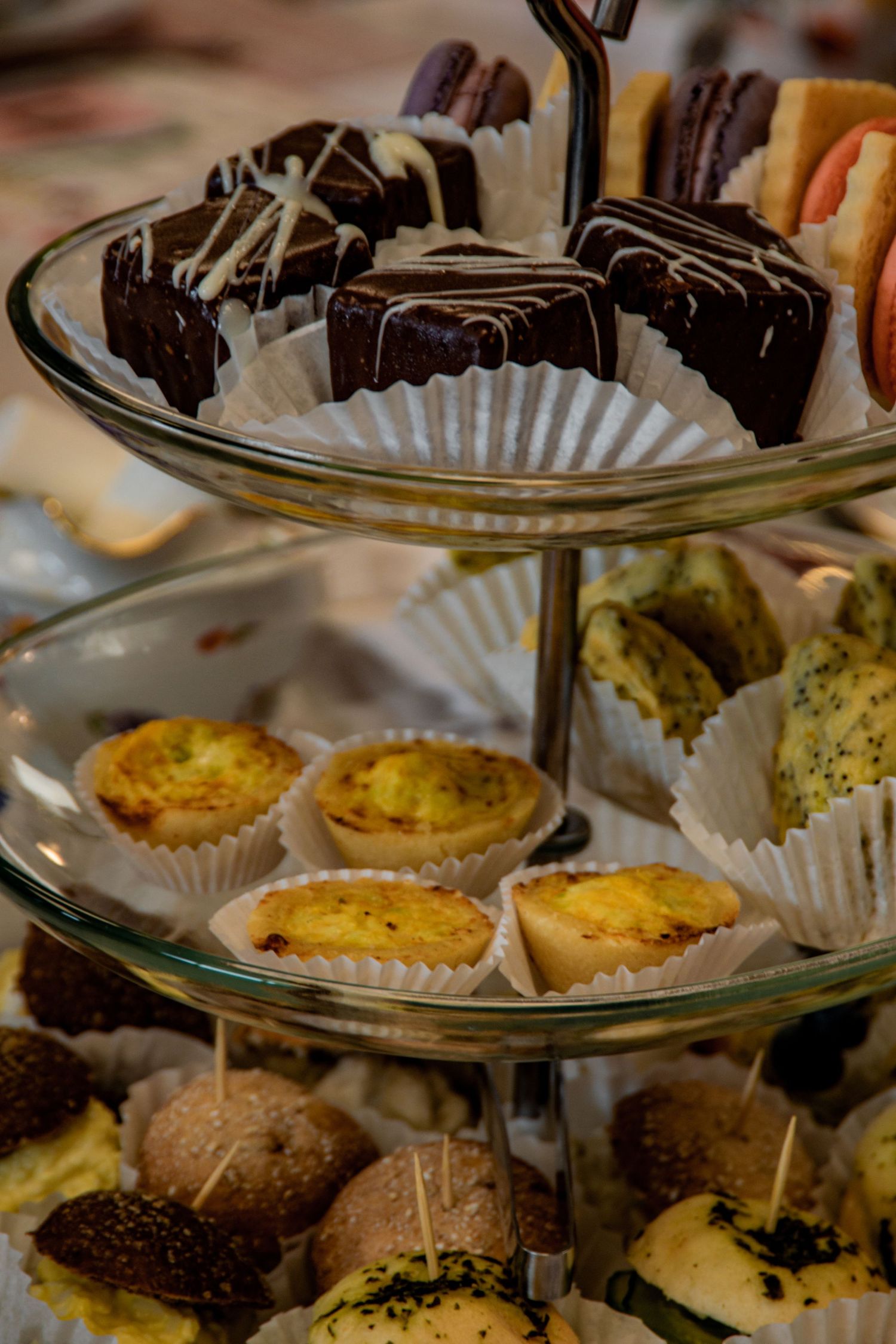 A tiered dessert stand displaying chocolate covered treats and mini quiches on paper liners.