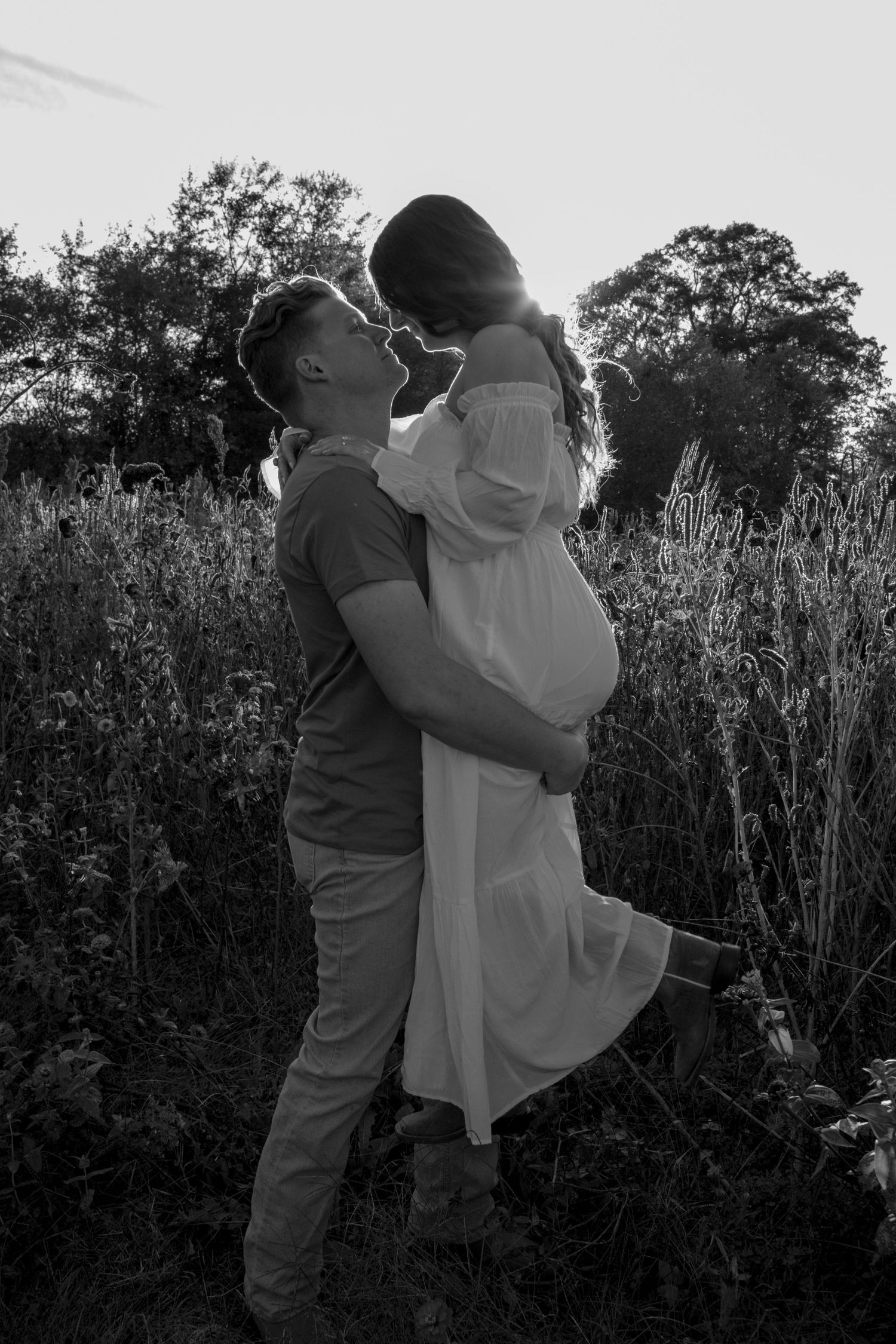 Black and white portrait of couple dancing in tall grass at dusk.