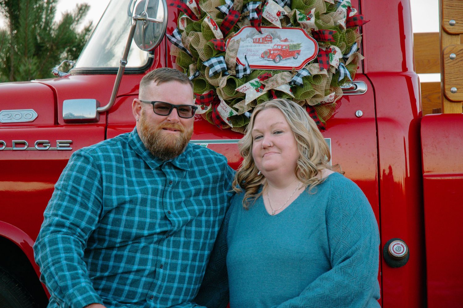 Couple embracing by vintage red truck with Christmas tree in background.