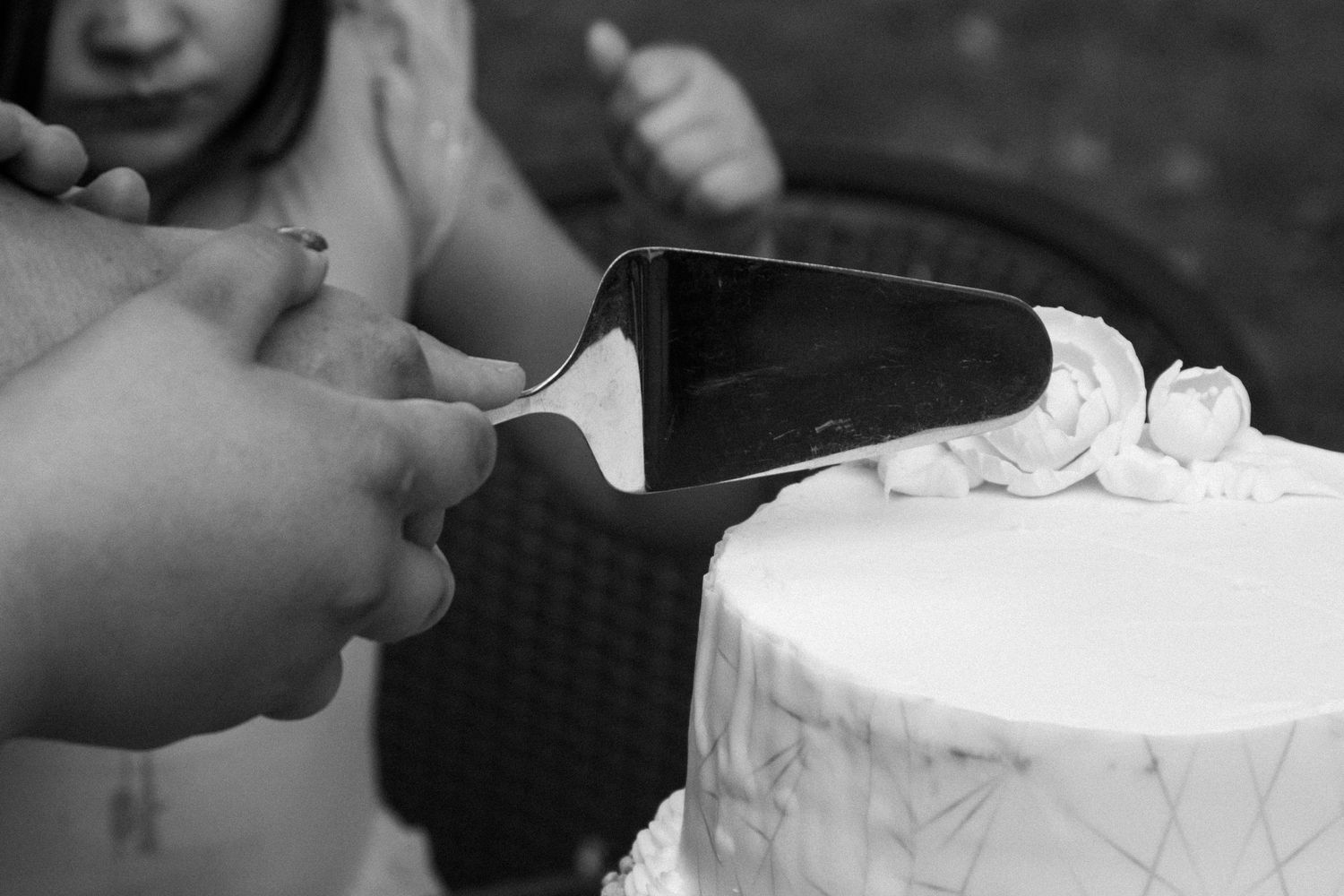 Close-up of hands cutting a white wedding cake with decorative frosting.