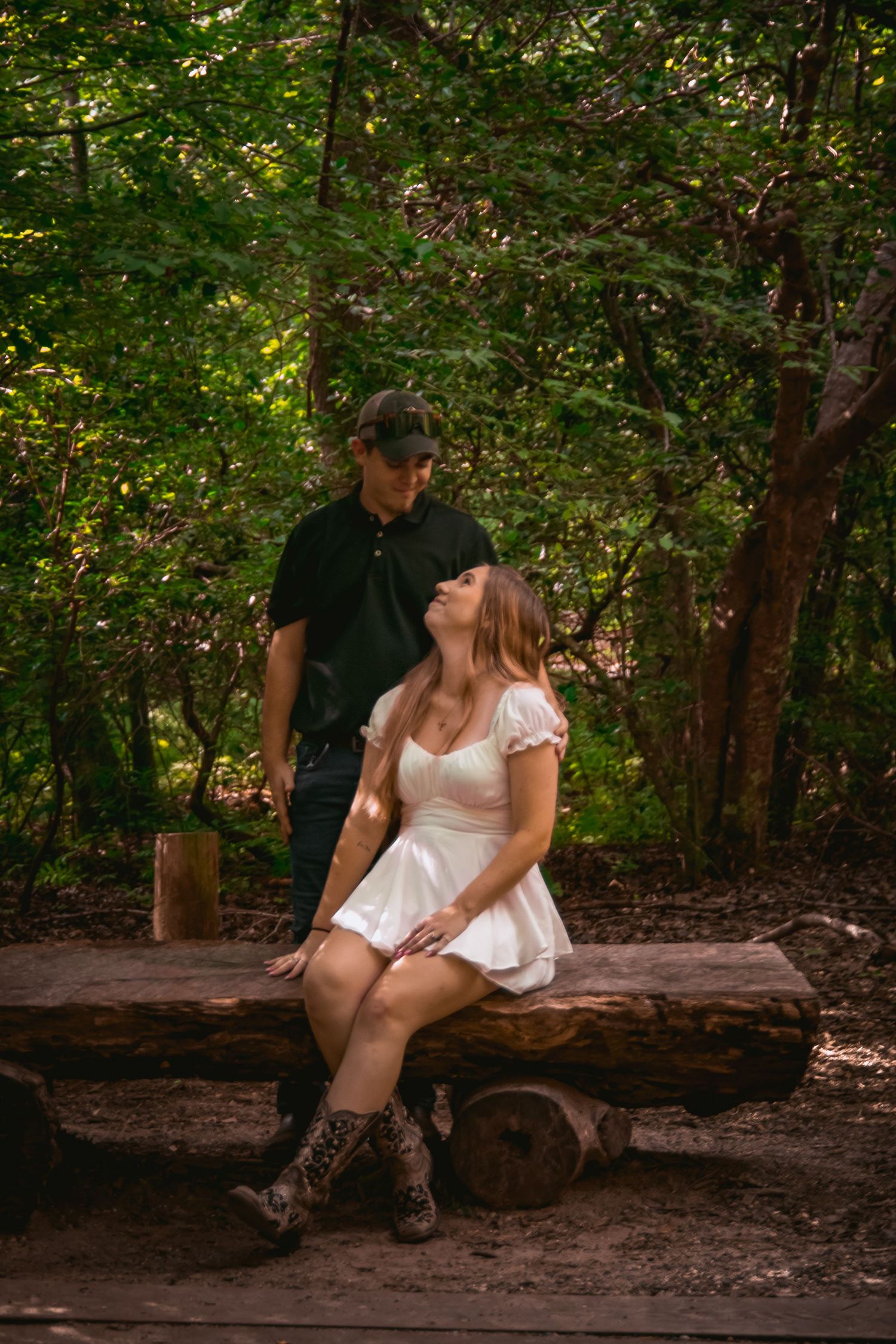 Couple sharing an intimate moment while sitting on a wooden log in a lush forest setting.