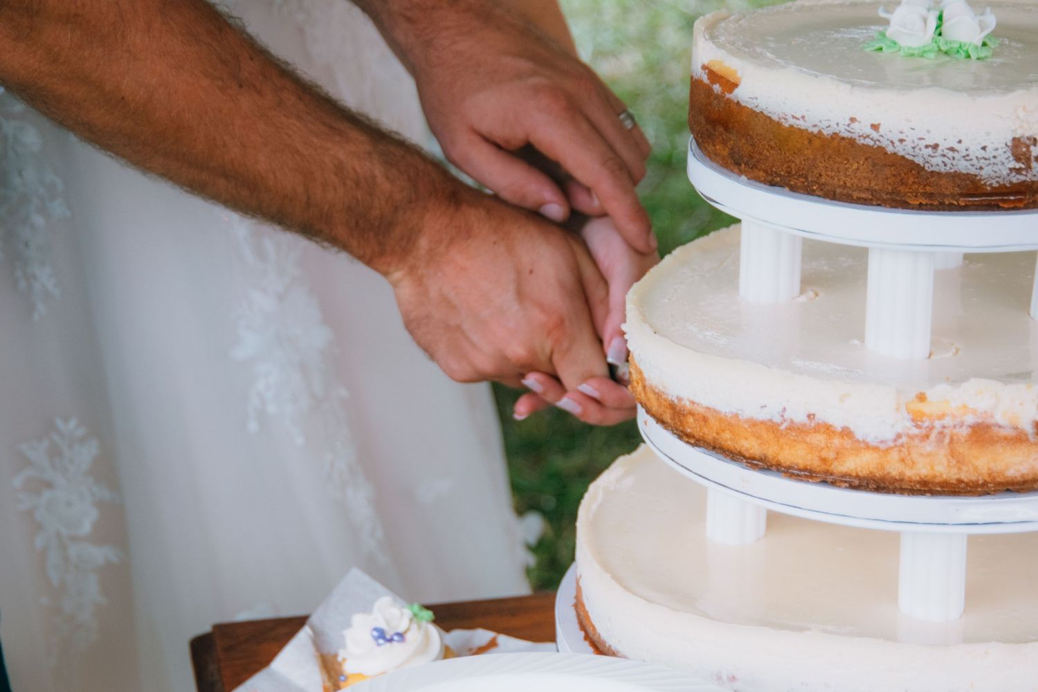 Hands assembling a tiered white wedding cake with delicate precision.
