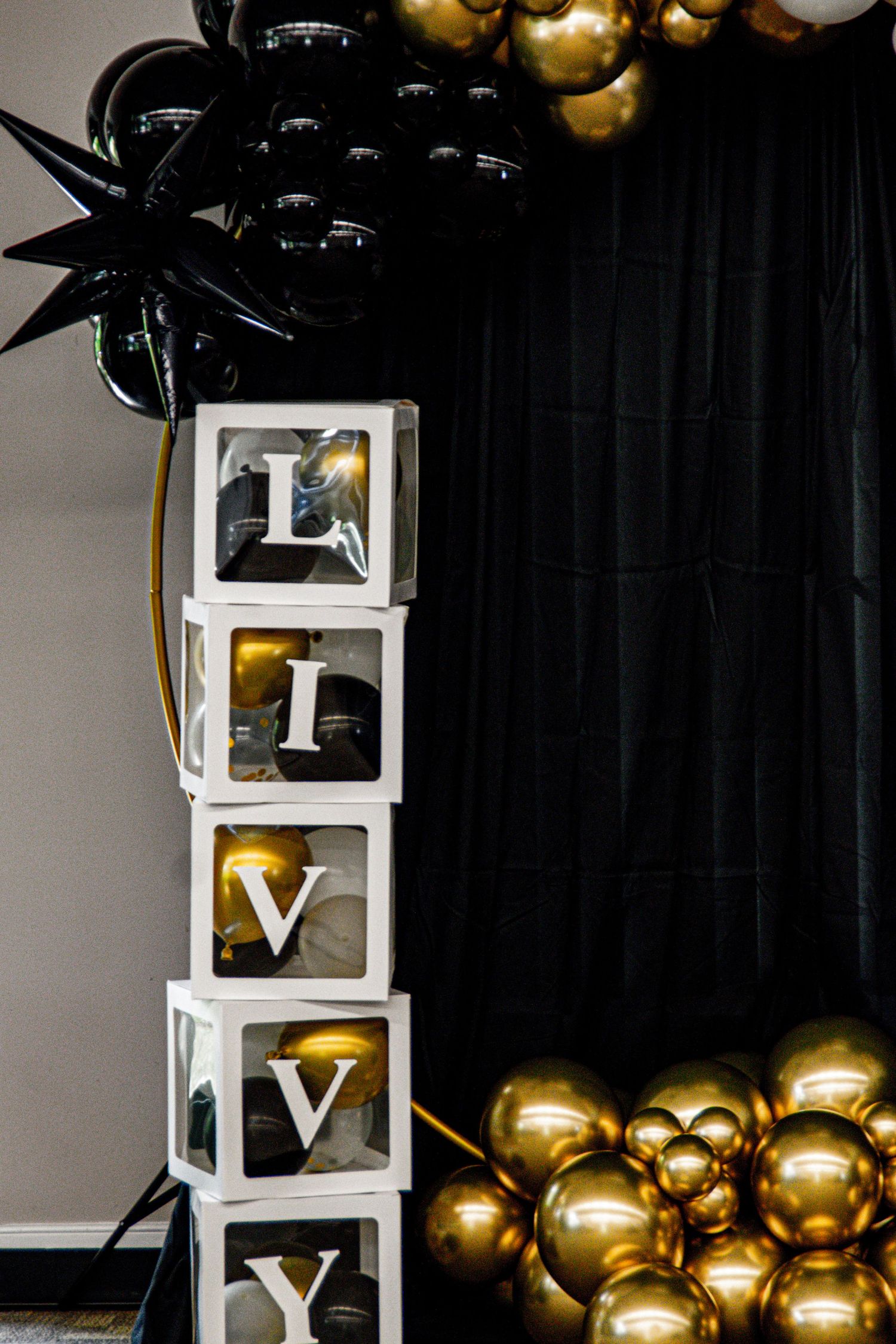 Modern event setup with illuminated white boxes and gold balloons against black backdrop.