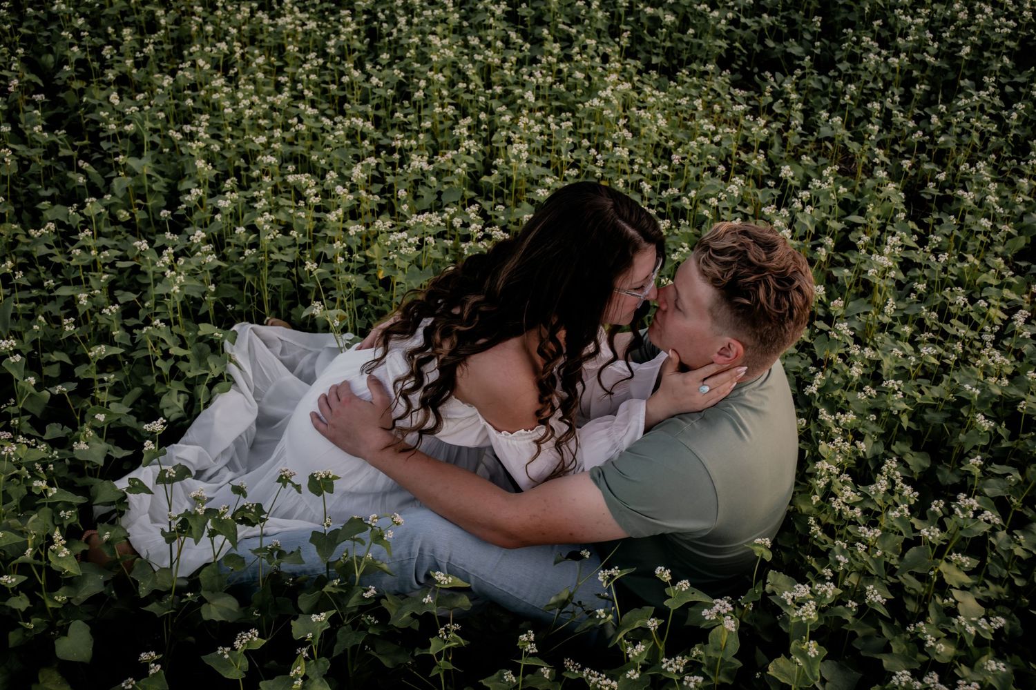 Romantic couple embracing in a field of white wildflowers during sunset.