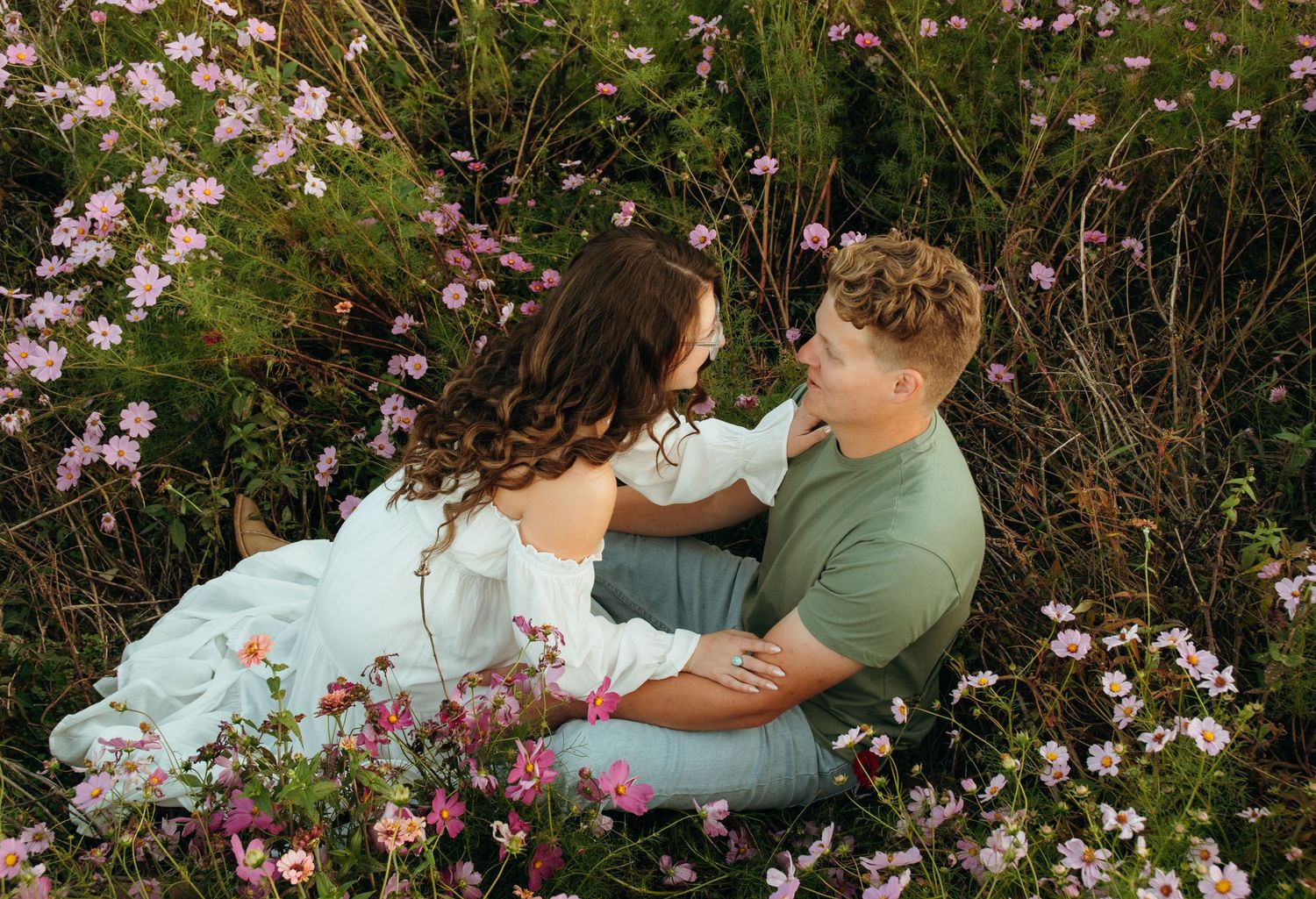Couple lounging together among pink cosmos flowers in garden setting.