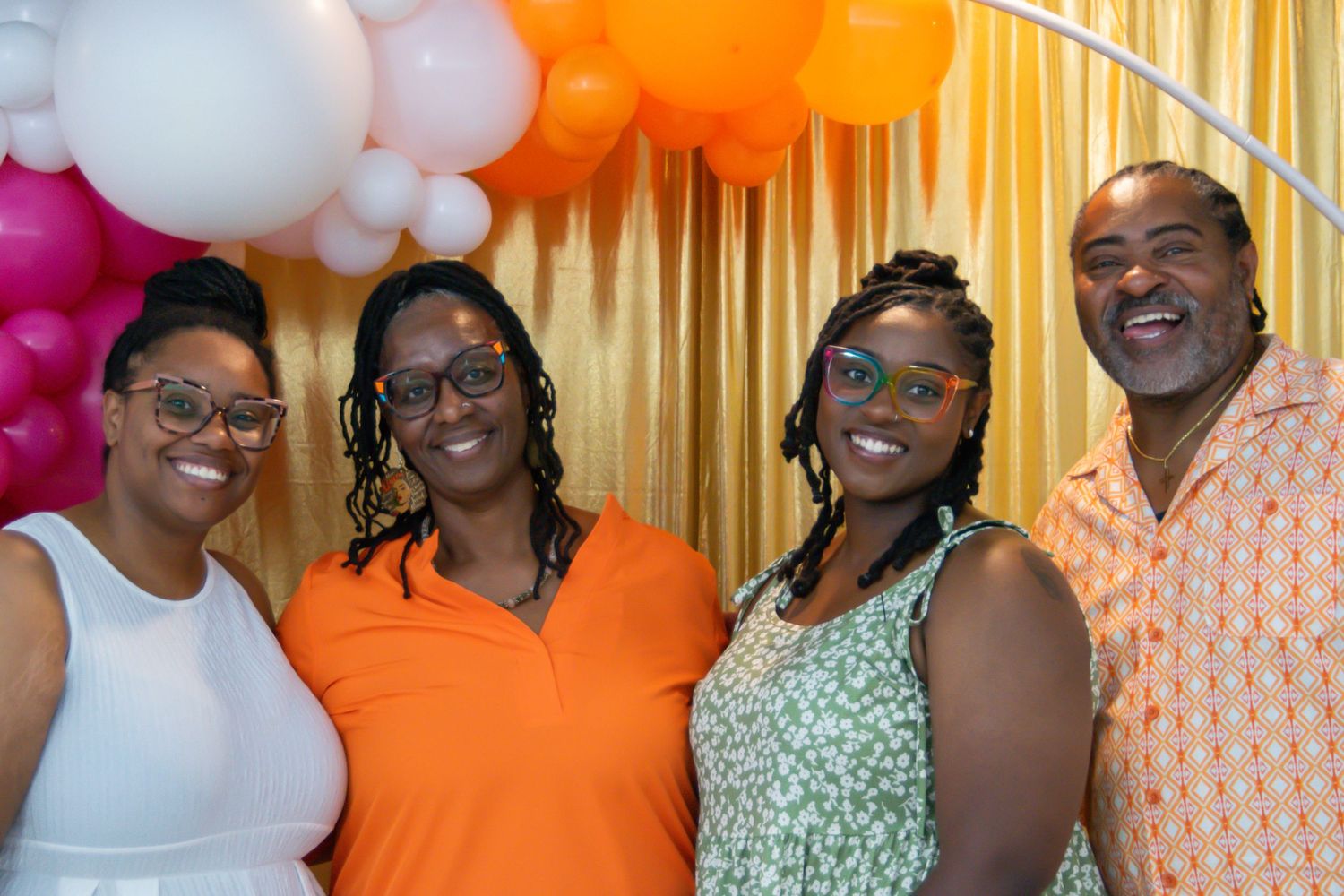 Group photo with colorful balloon arch featuring orange, pink and white decorations.