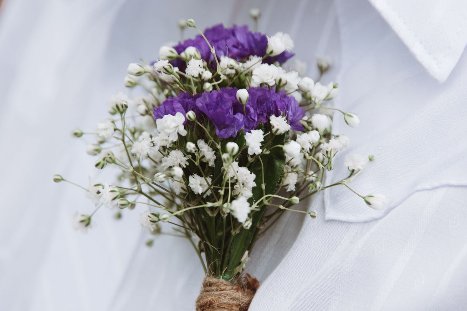 Purple and white wildflowers arranged in rustic glass vases against a light background.