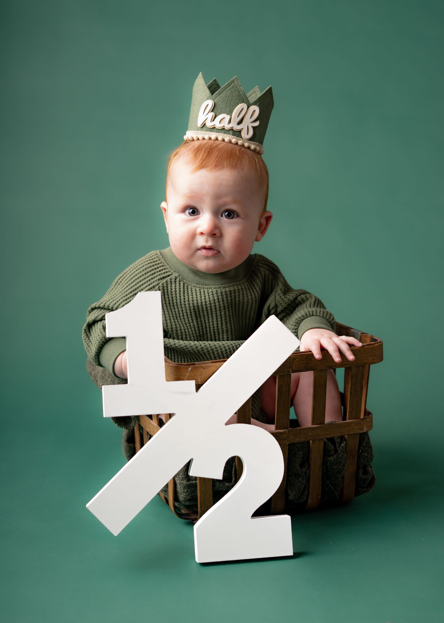 Baby milestone session in green monochromatic look baby looking at camera in vintage basket