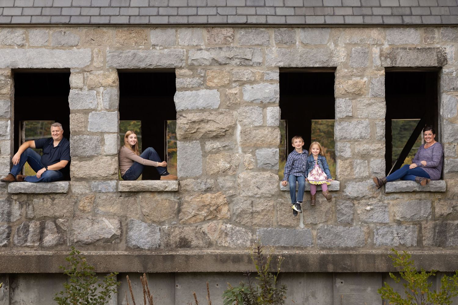Several people peer out through small windows in an old stone building wall.