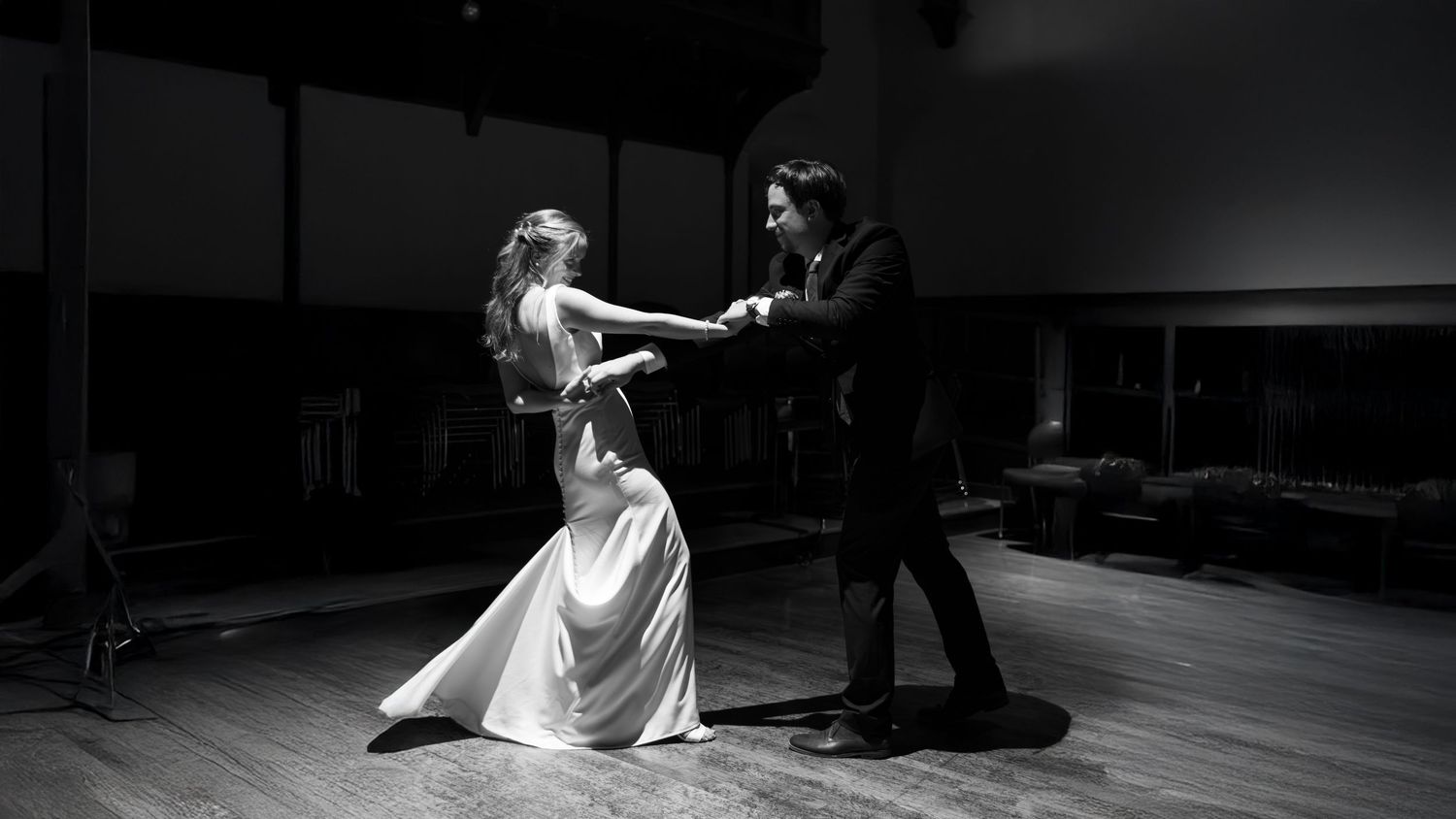 A couple performs an elegant ballroom dance in black and white on a wooden dance floor.