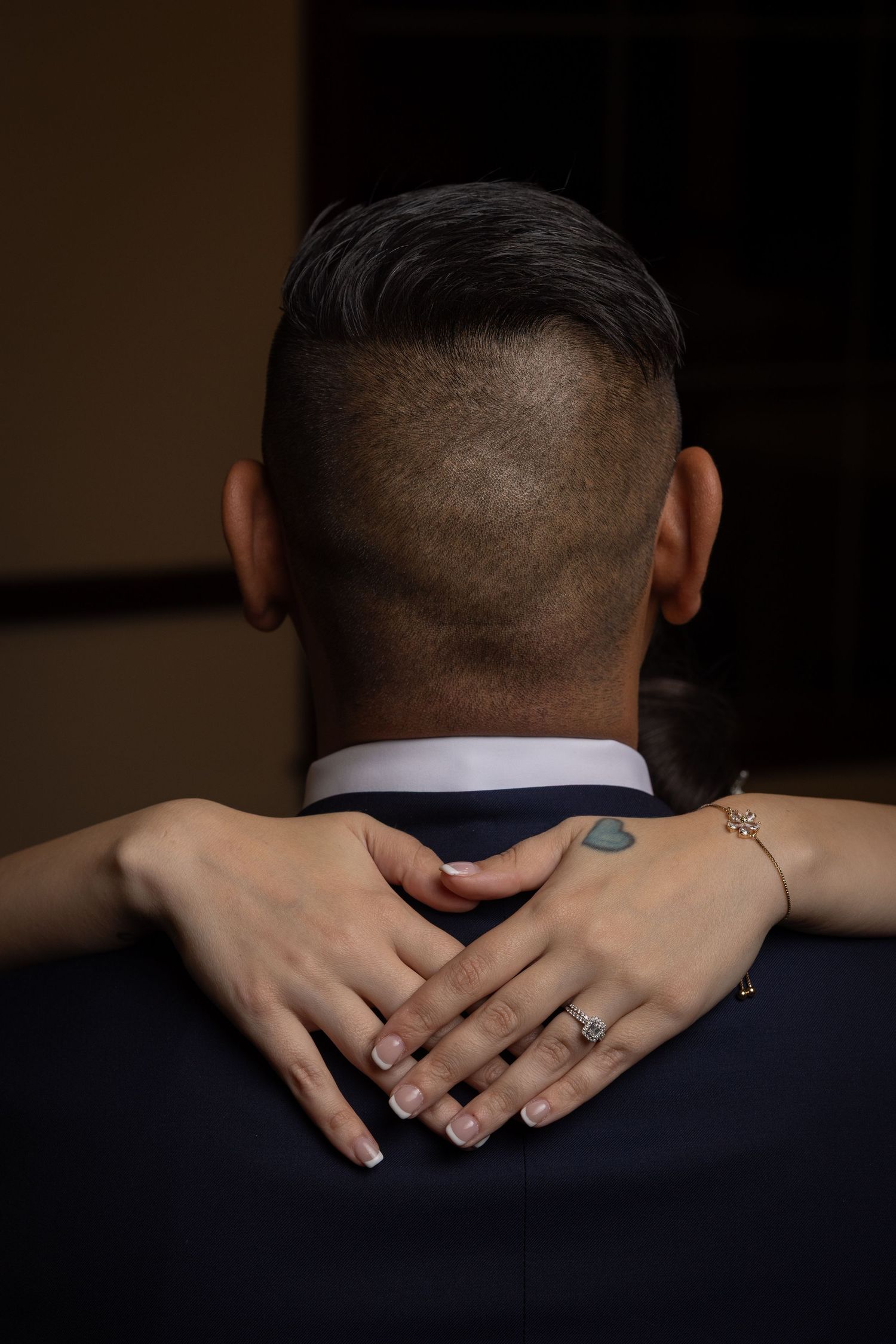 Close-up view of hands embracing the back of a neck against a dark navy suit background.