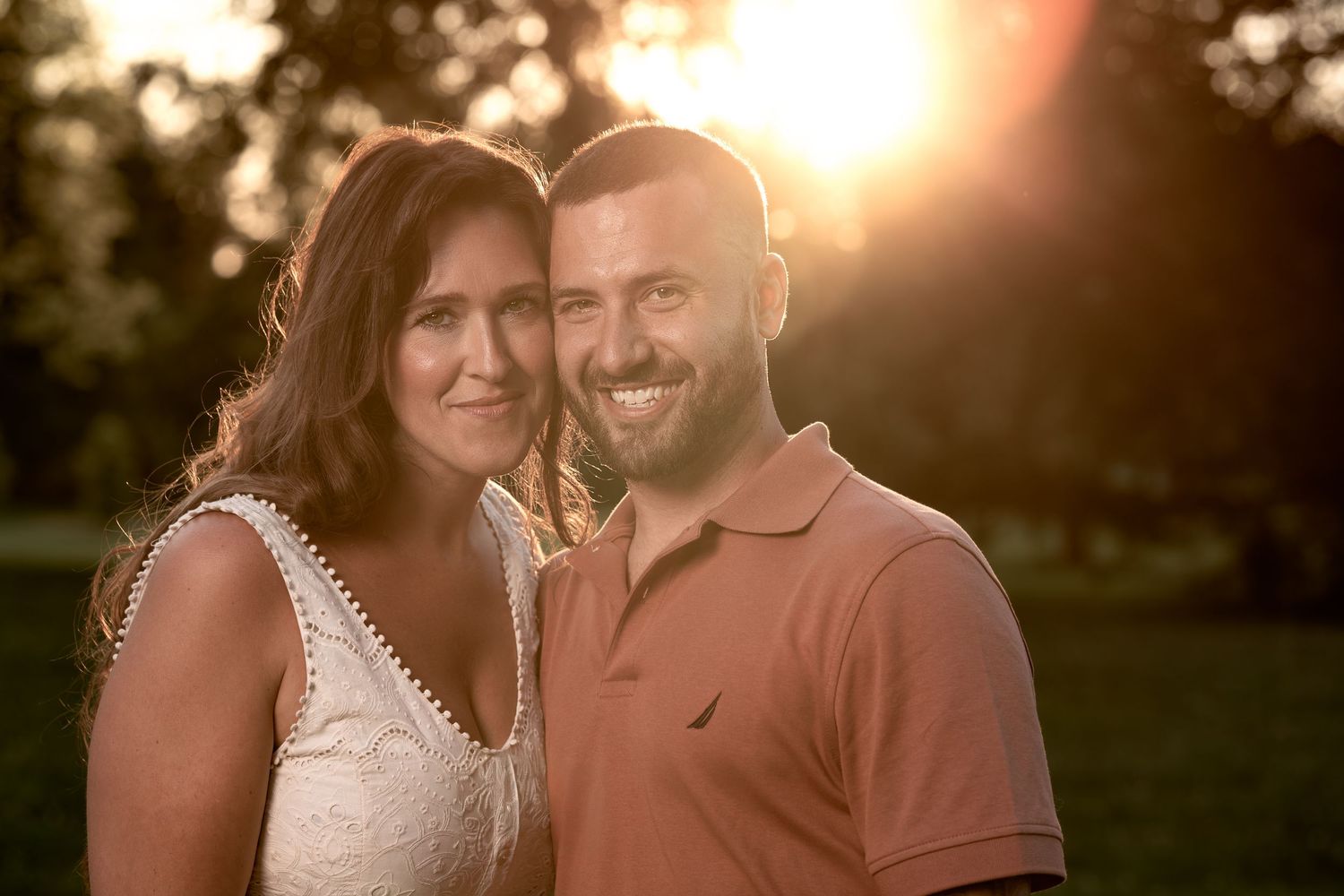 A couple embraces during a golden sunset photoshoot in a romantic outdoor setting.