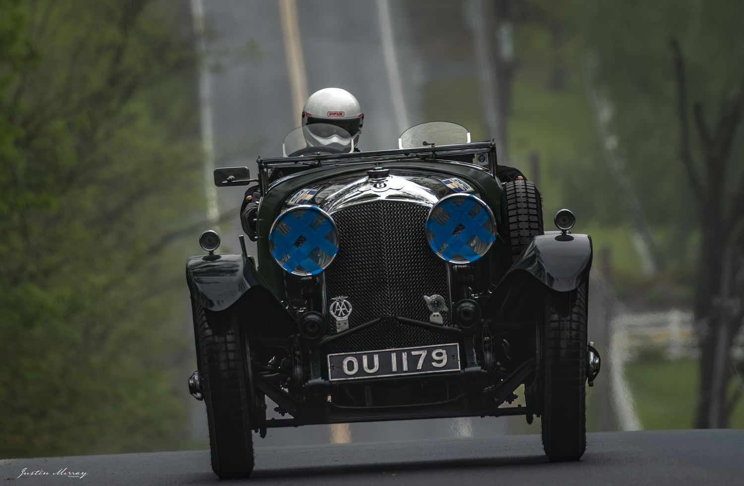 Vintage black sports car photographed in motion from multiple angles on a tree-lined road.